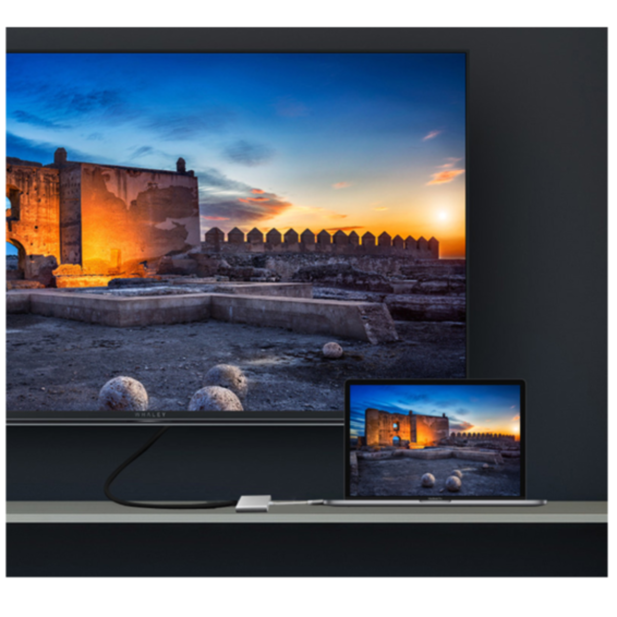 Schermo TV che mostra un tramonto su una città antica e un laptop con la stessa scena.