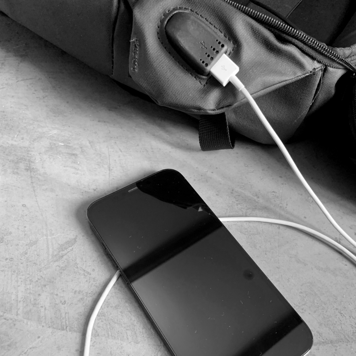 Mochila negra y gris con un teléfono cargando. El teléfono está en el suelo.