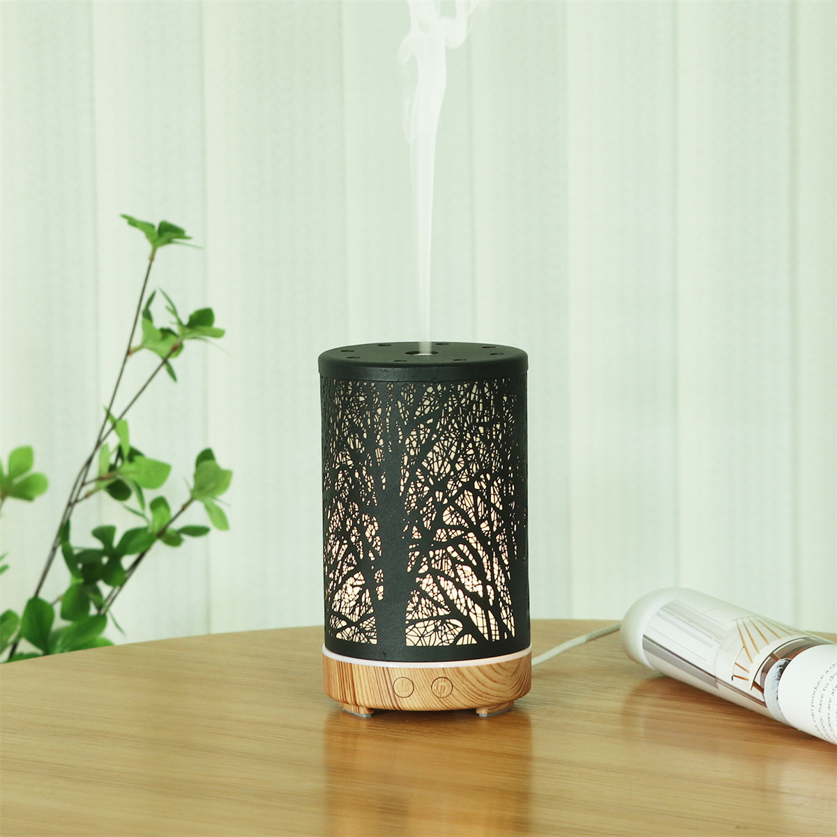 Schwarzer und silberner Aromatherapie-Diffusor mit Baumdesign, weißem Dampf, auf Holztisch.