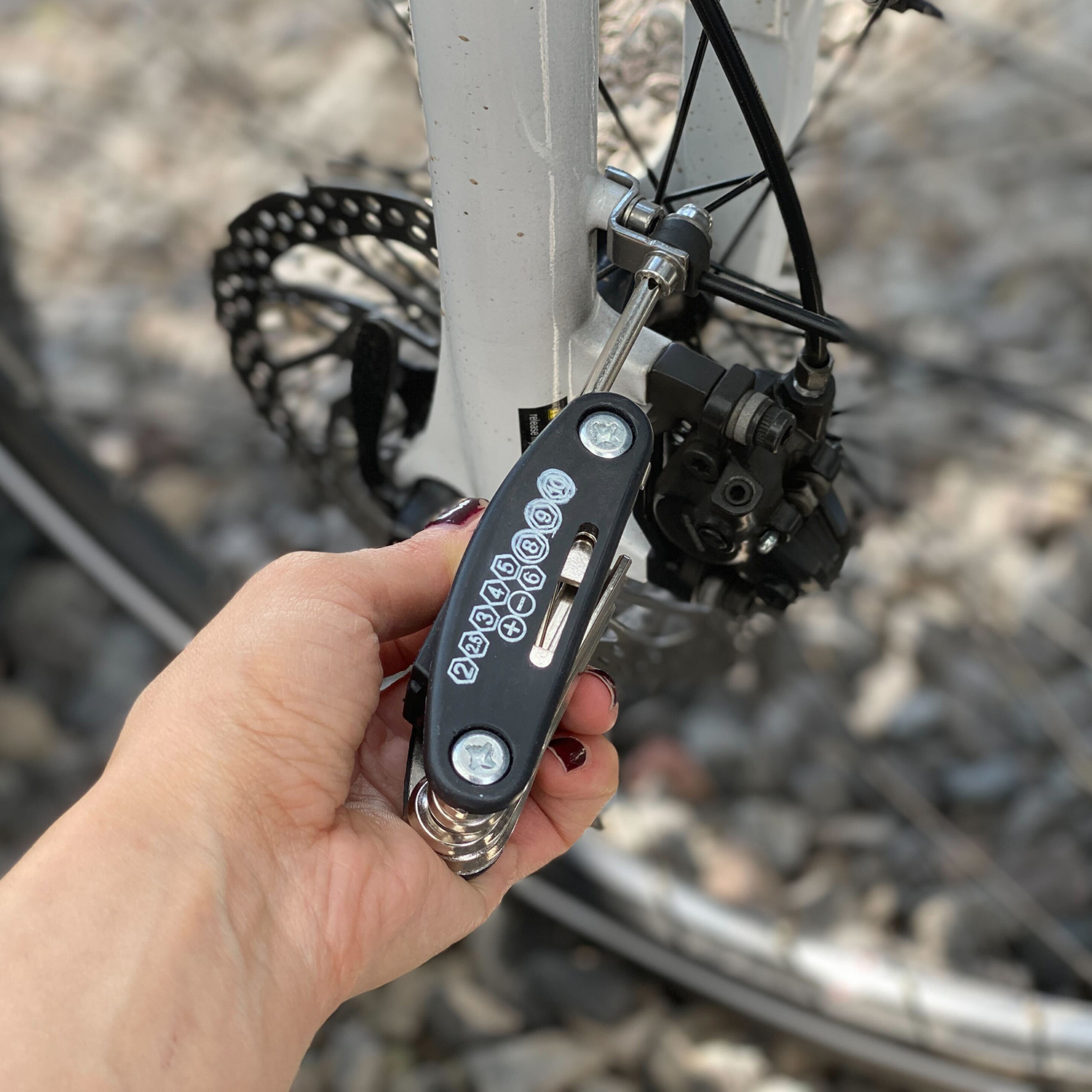 Hand hält ein schwarzes Multi-Tool neben einem Fahrradrad und einer Bremse.