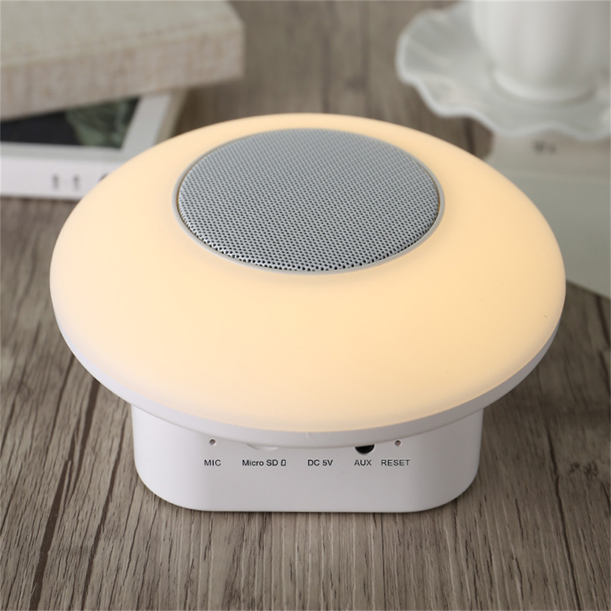 Eine weiße pilzförmige Lampe mit einem Lautsprecher oben. Sie leuchtet mit warmem Licht.