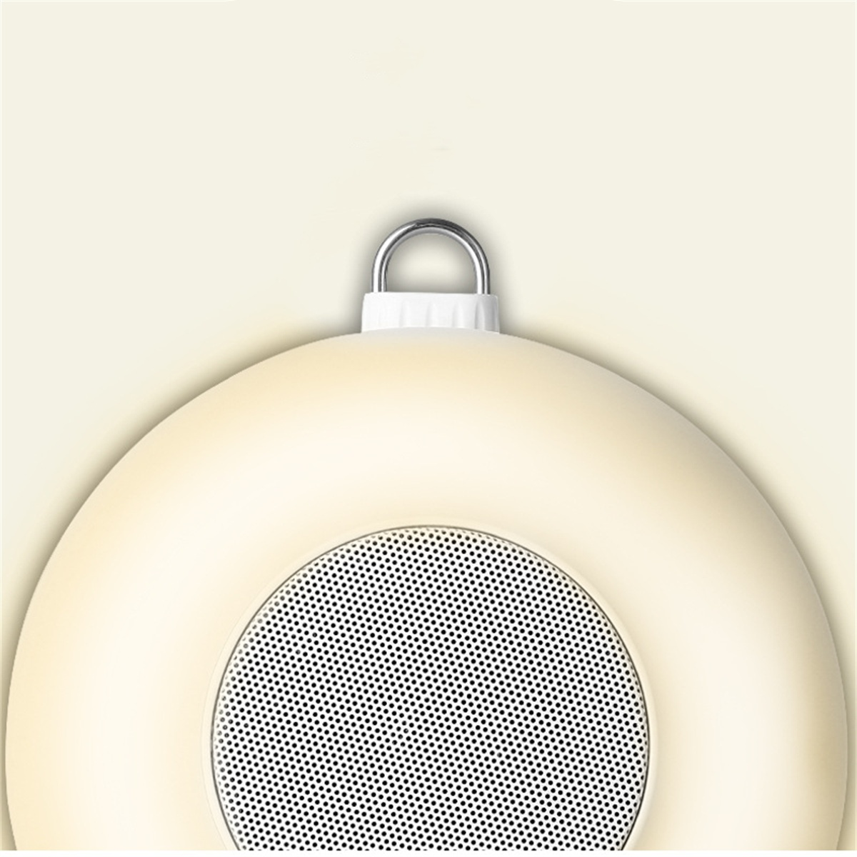 Cremefarbener Lautsprecher mit Mesh-Gitter, Ringschlaufe und weißer Basis. Ein hellbeiger Hintergrund.