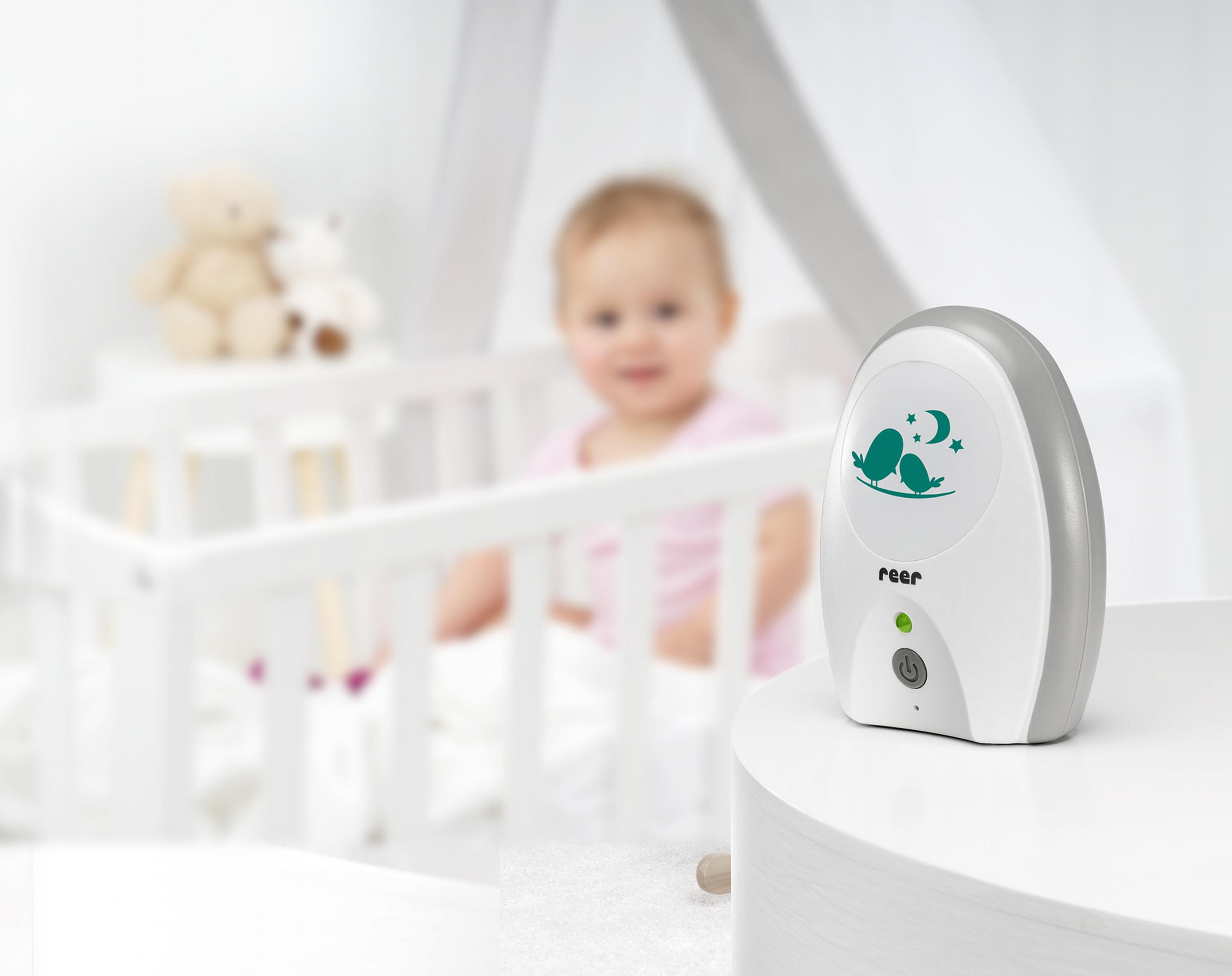 Niania elektroniczna na stole z łóżeczkiem dziecięcym w rozmytym tle.