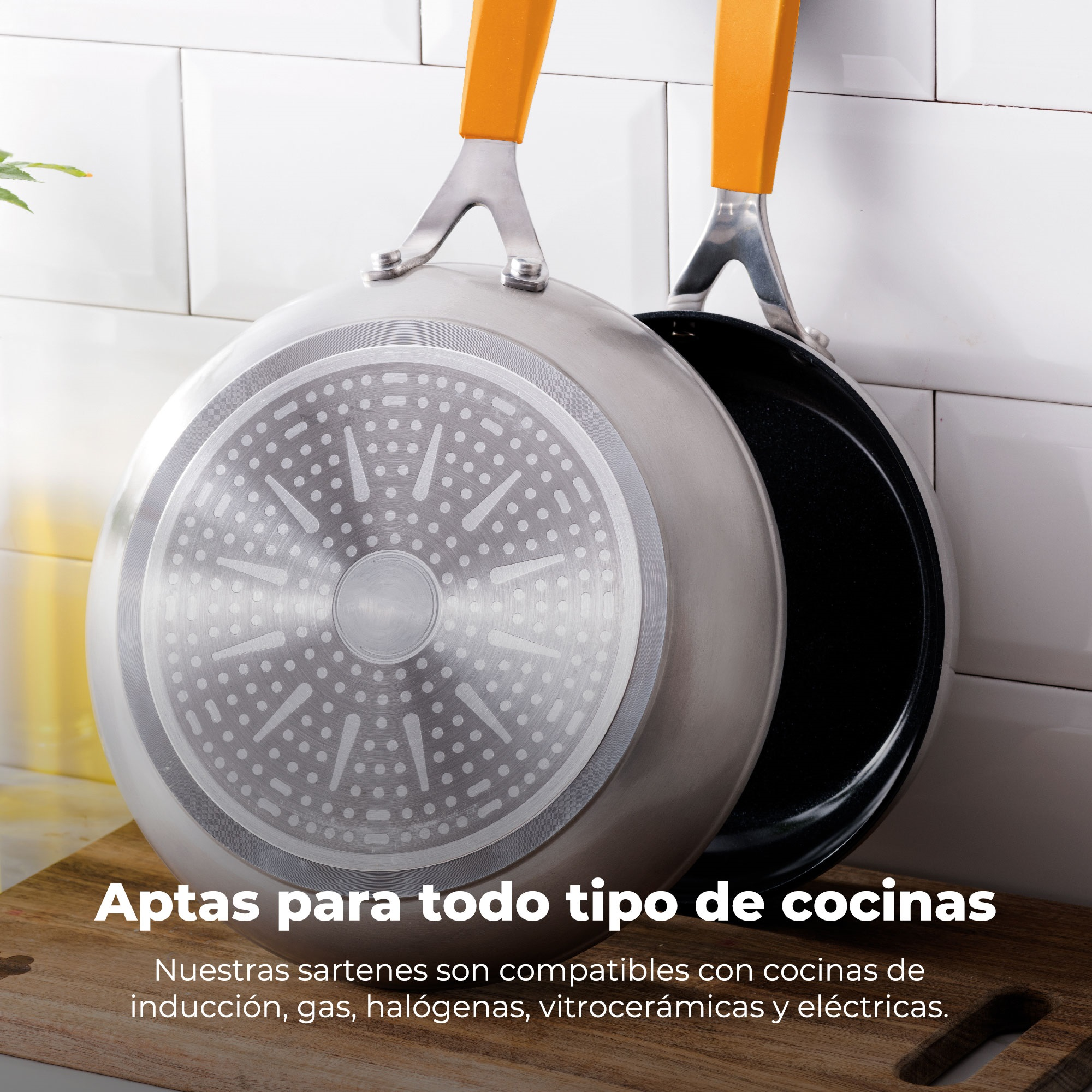 Dos sartenes colgantes con asas naranjas. Una muestra la parte inferior con puntos plateados y blancos, la otra es negra por dentro.