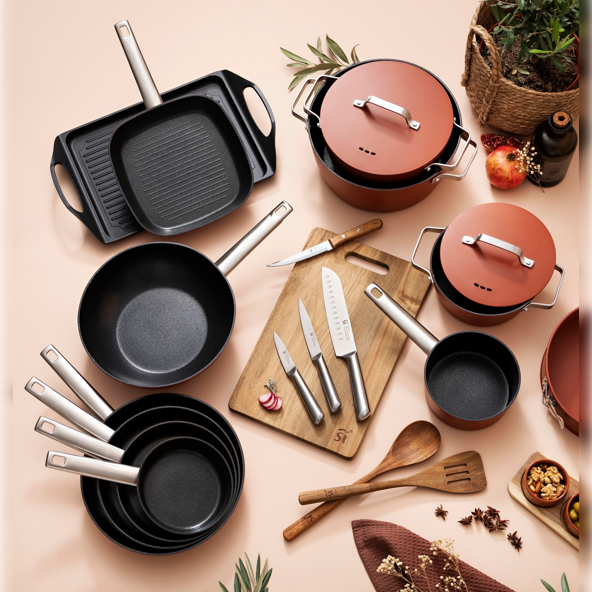 Vista superior de varios utensilios de cocina. Sartenes, ollas, cuchillos, tabla de cortar y cucharas de madera están dispuestas sobre una superficie clara.