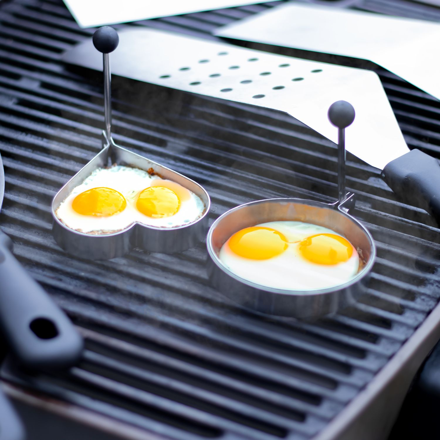 Eier werden auf einem Grill gebraten. Zwei Eier in Herz- und runden Formen.