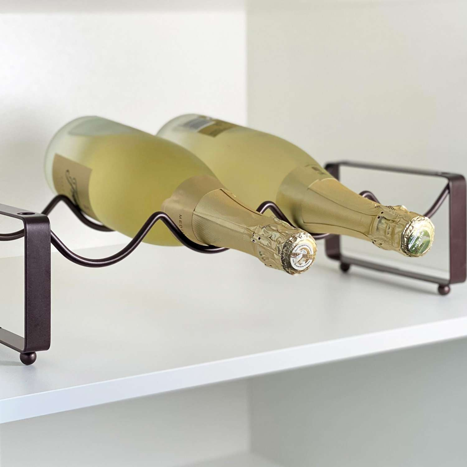 Zwei Champagnerflaschen in einem Weinregal. Das Regal ist braun, die Flaschen sind gold und grün.