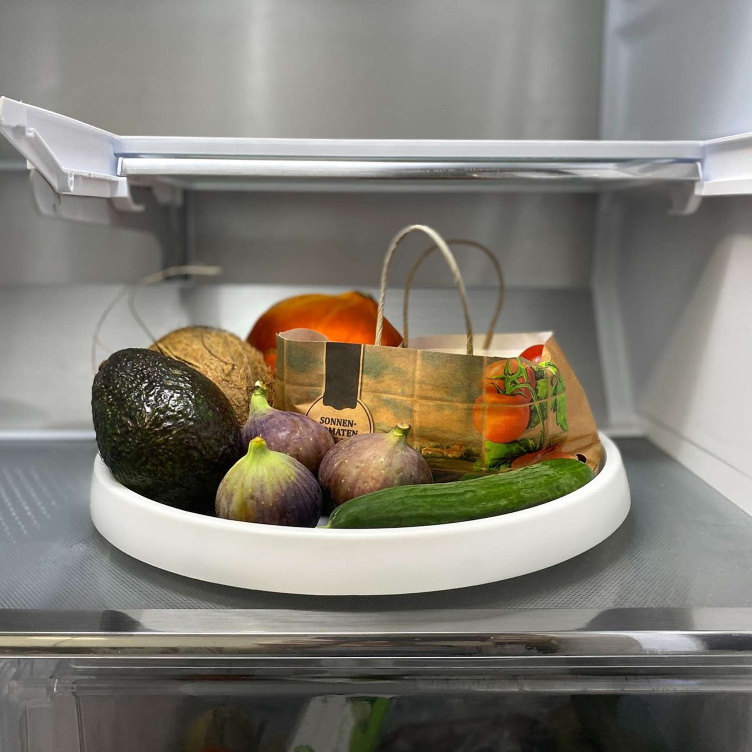 Tablett im Kühlschrank mit Feigen, Avocado, Gurke, Tüte und Kokosnuss. Frische Produkte ausgestellt.