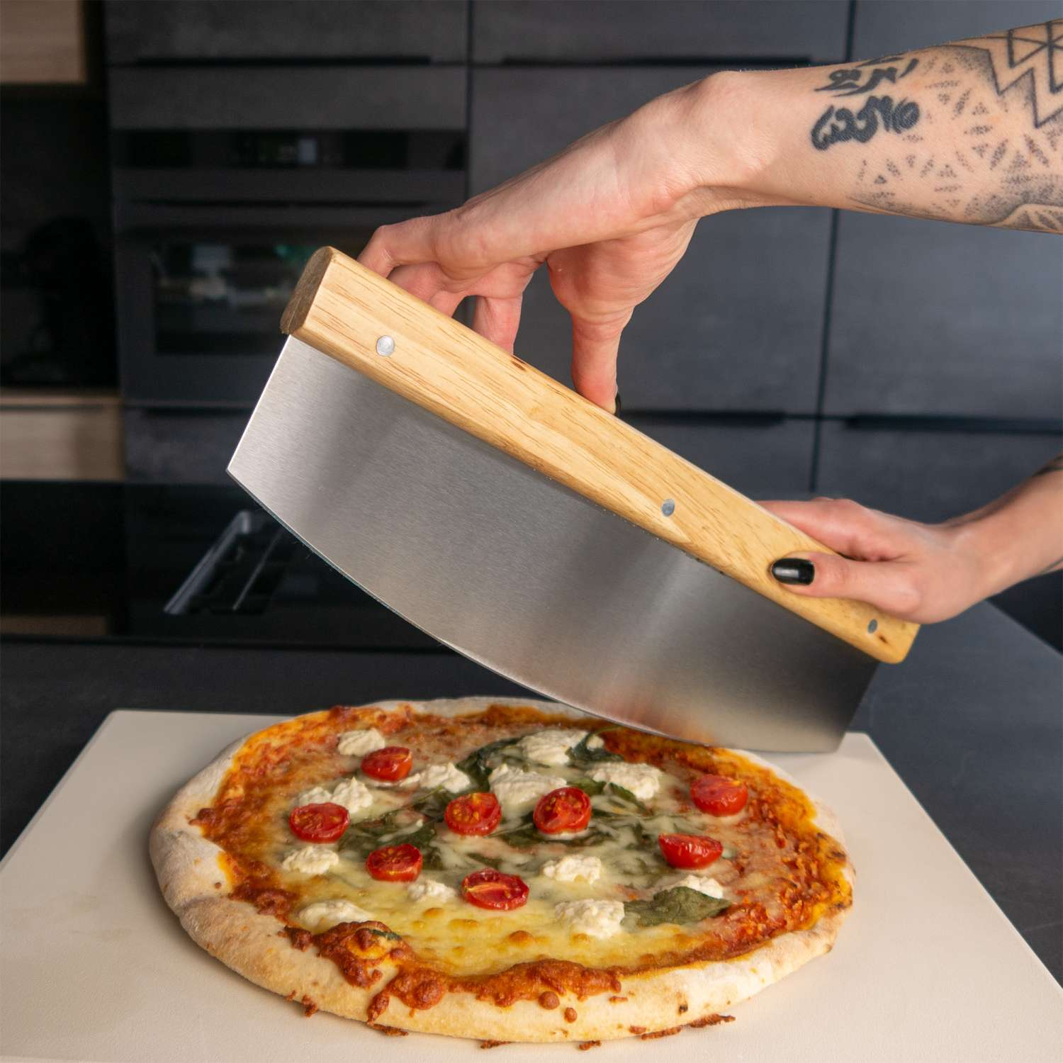 Eine Pizza wird mit einem Pizzaschneider geschnitten. Die Pizza hat Tomaten und Basilikum darauf.