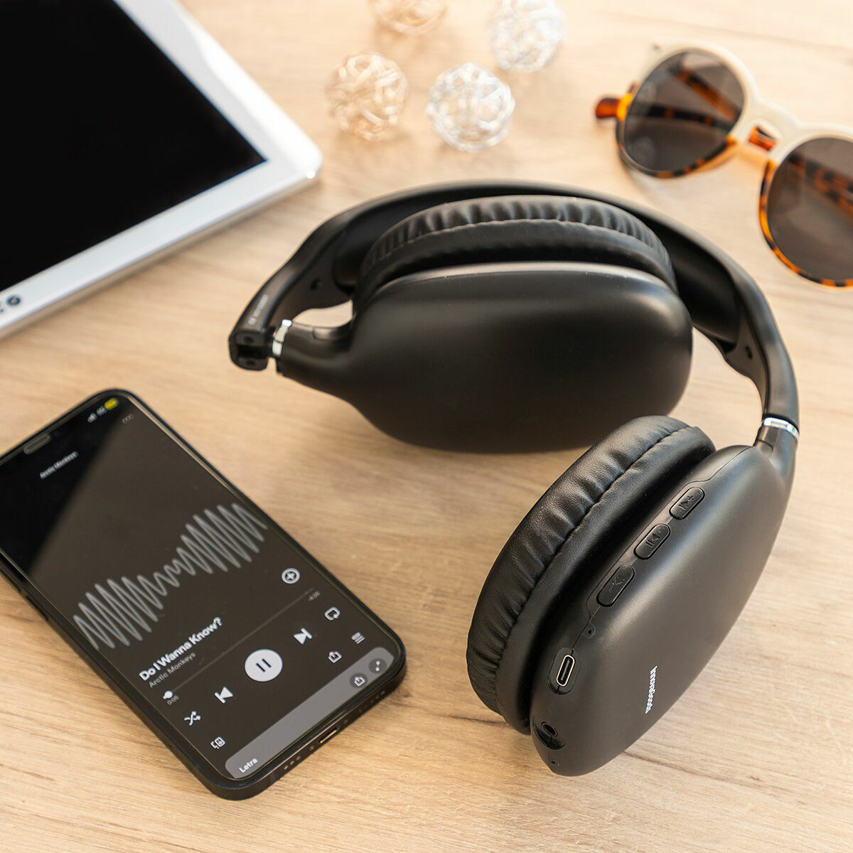 Uno smartphone che riproduce musica, un paio di cuffie, occhiali da sole e palline decorative su una superficie di legno.