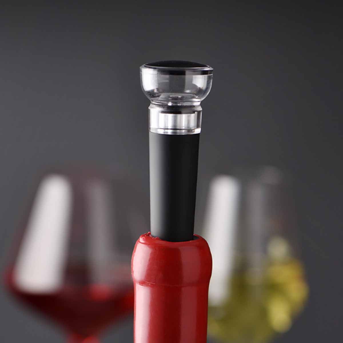 Weinflasche mit Stöpsel. Flasche ist rot, Stöpsel schwarz und klar. Ein Weinglas ist im Hintergrund unscharf.