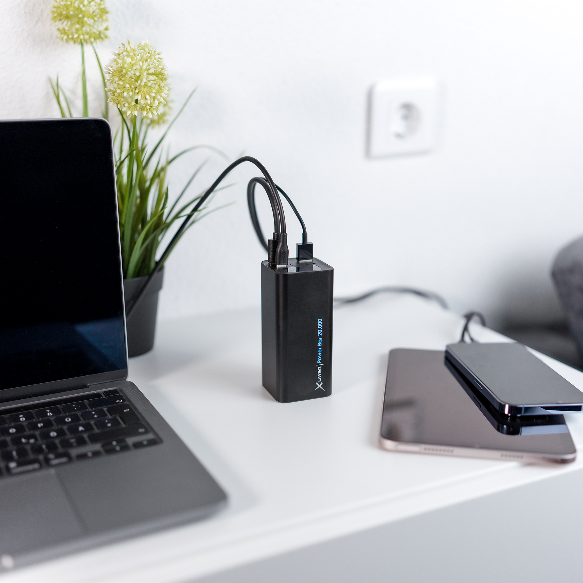 Eine schwarze Powerbank mit Laptop, Telefon und Tablet, die auf einer weißen Oberfläche geladen werden.