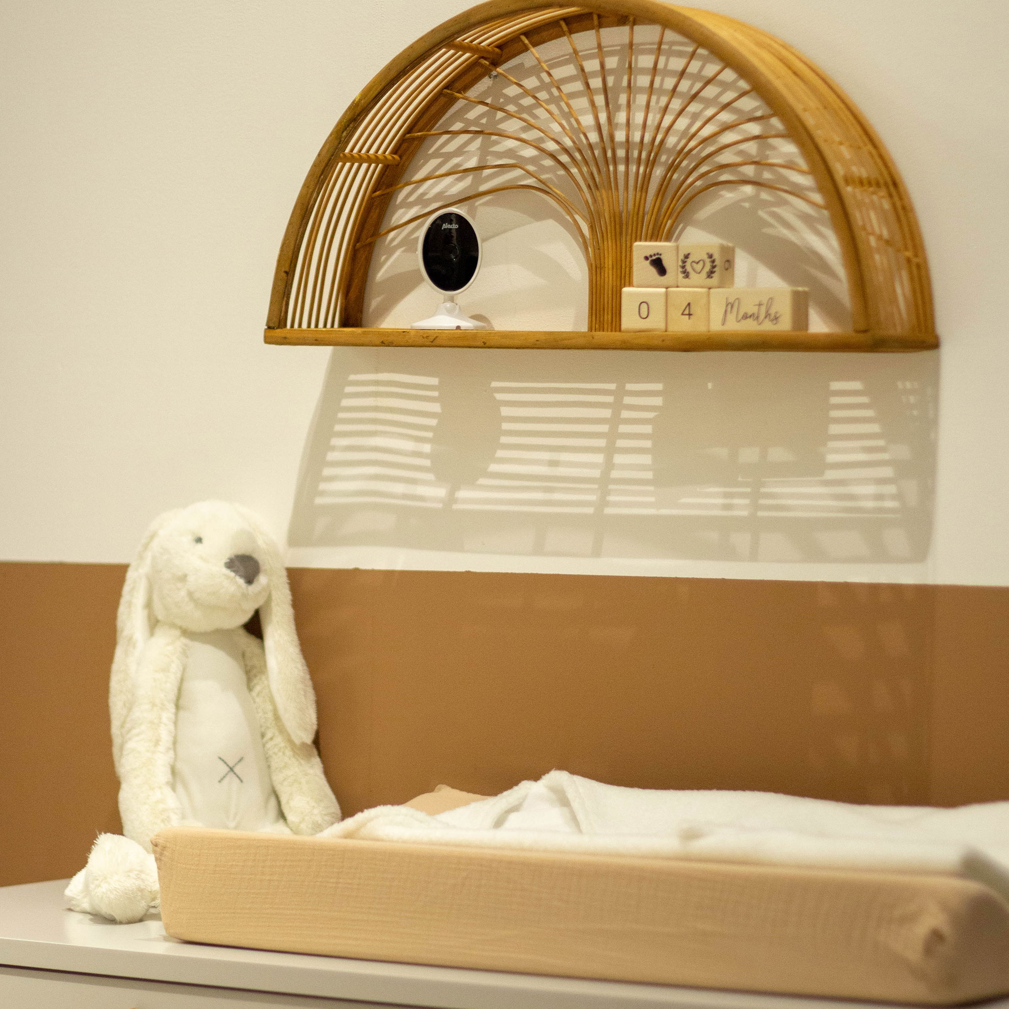 Ein Babyzimmer mit Regal, Plüschtier und Wickelauflage. Weiche Farben.