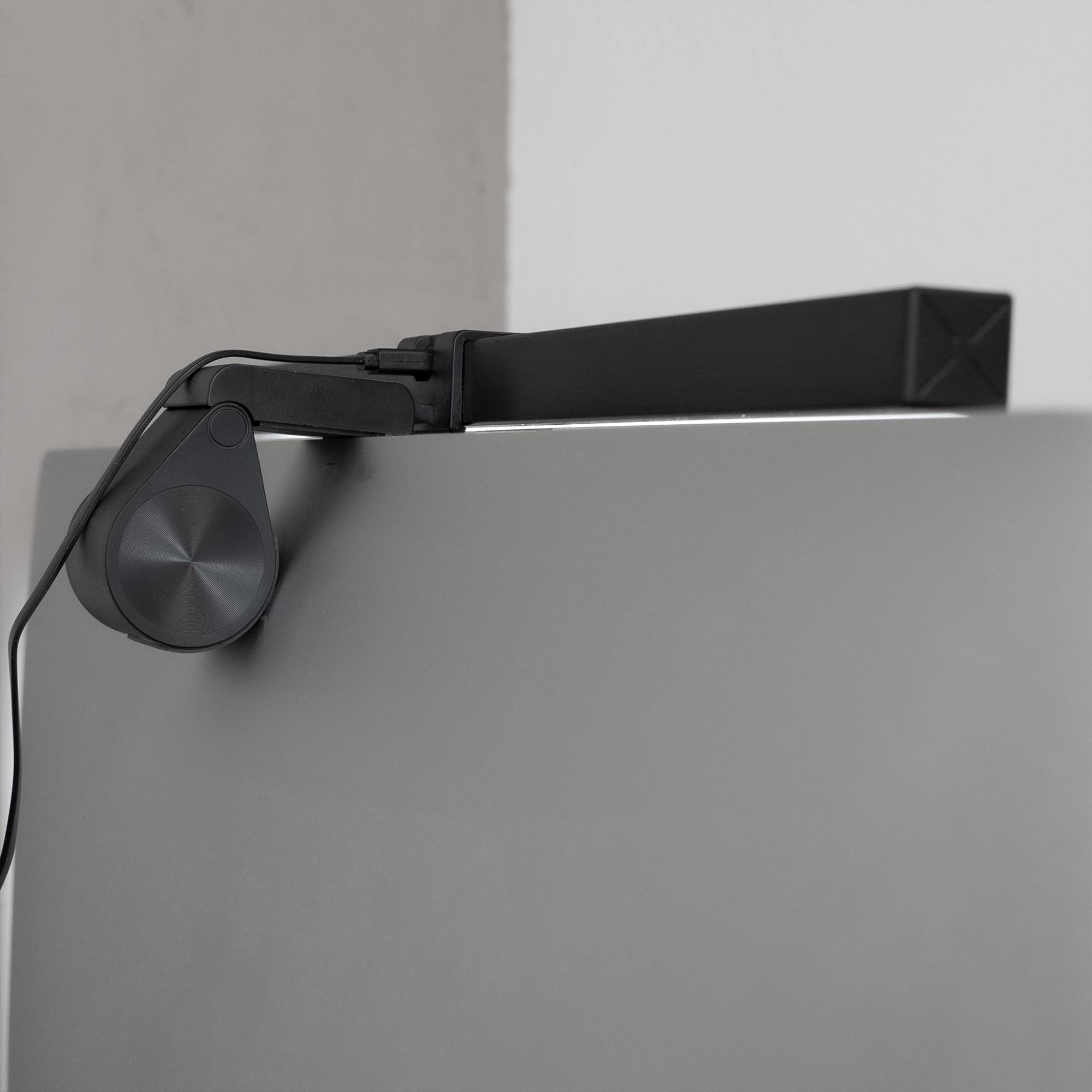 Eine schwarze LED-Schreibtischlampe auf einer grauen Oberfläche montiert. Licht wird von der Lampe emittiert.
