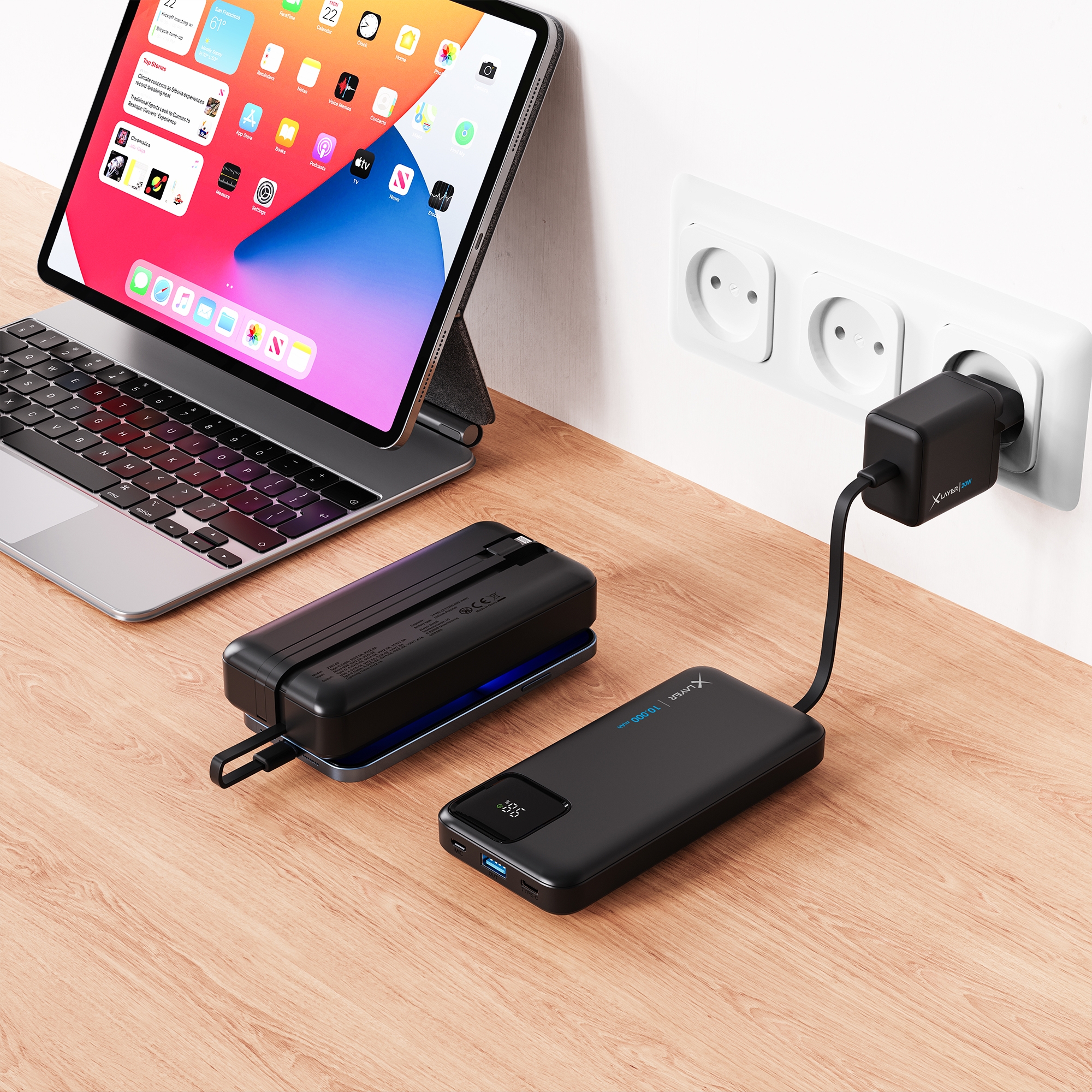 Tablet, schwarze Powerbank, Ladegerät in der Steckdose, auf einem Holztisch.