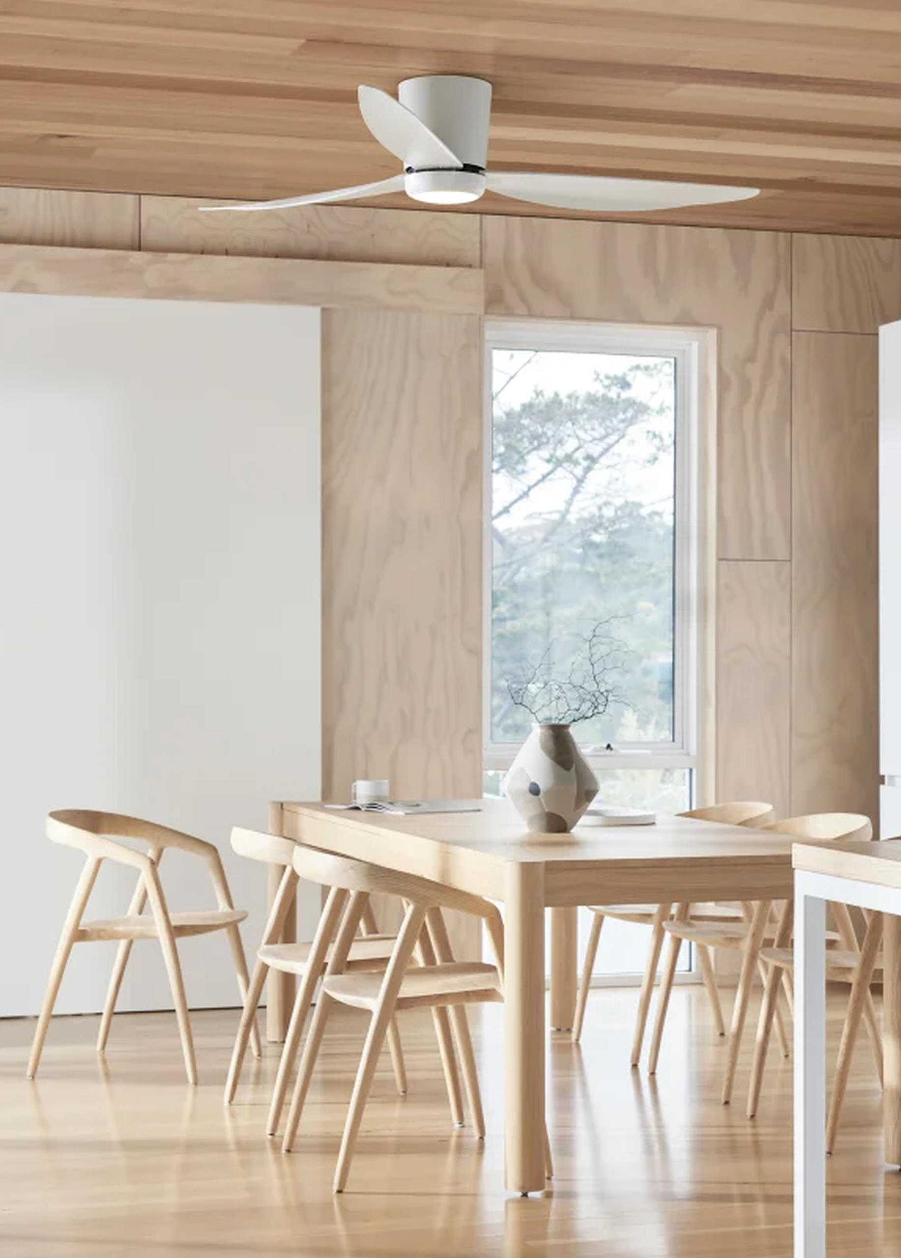 Ein Esszimmer mit einem Holztisch, Stühlen und einem Deckenventilator. Ein Fenster zeigt eine Aussicht auf Bäume.