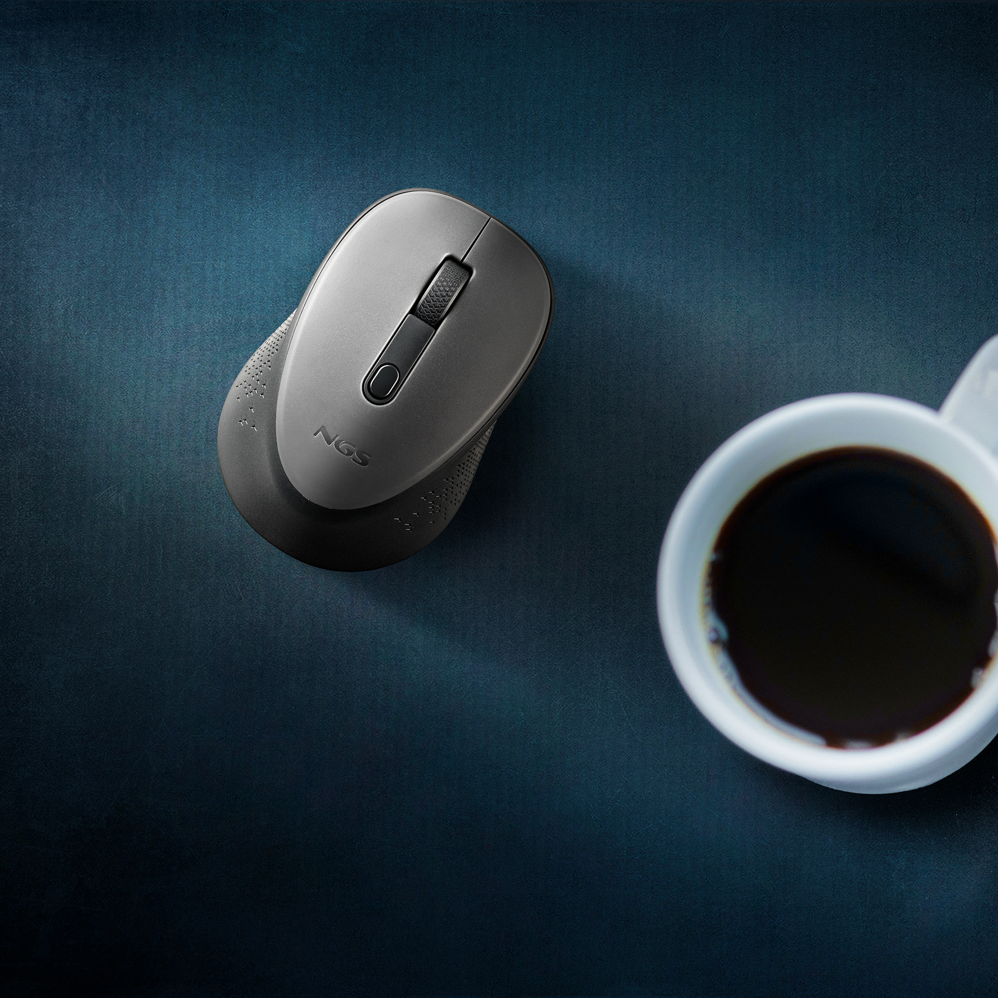 Kabellose Maus auf dunkler Oberfläche, Kaffeetasse rechts.