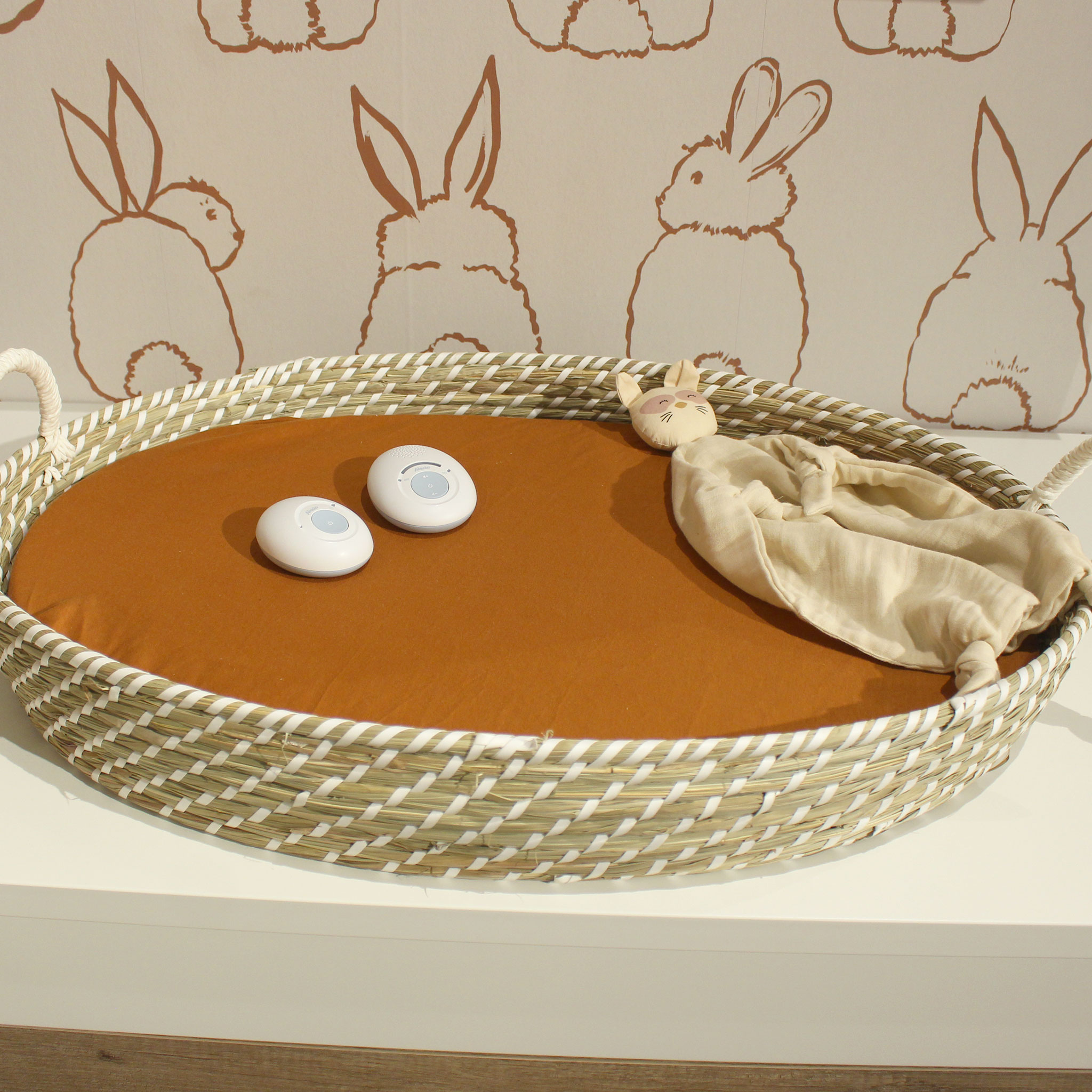 A baby changing basket with items inside. A white surface and a bunny themed wall.
