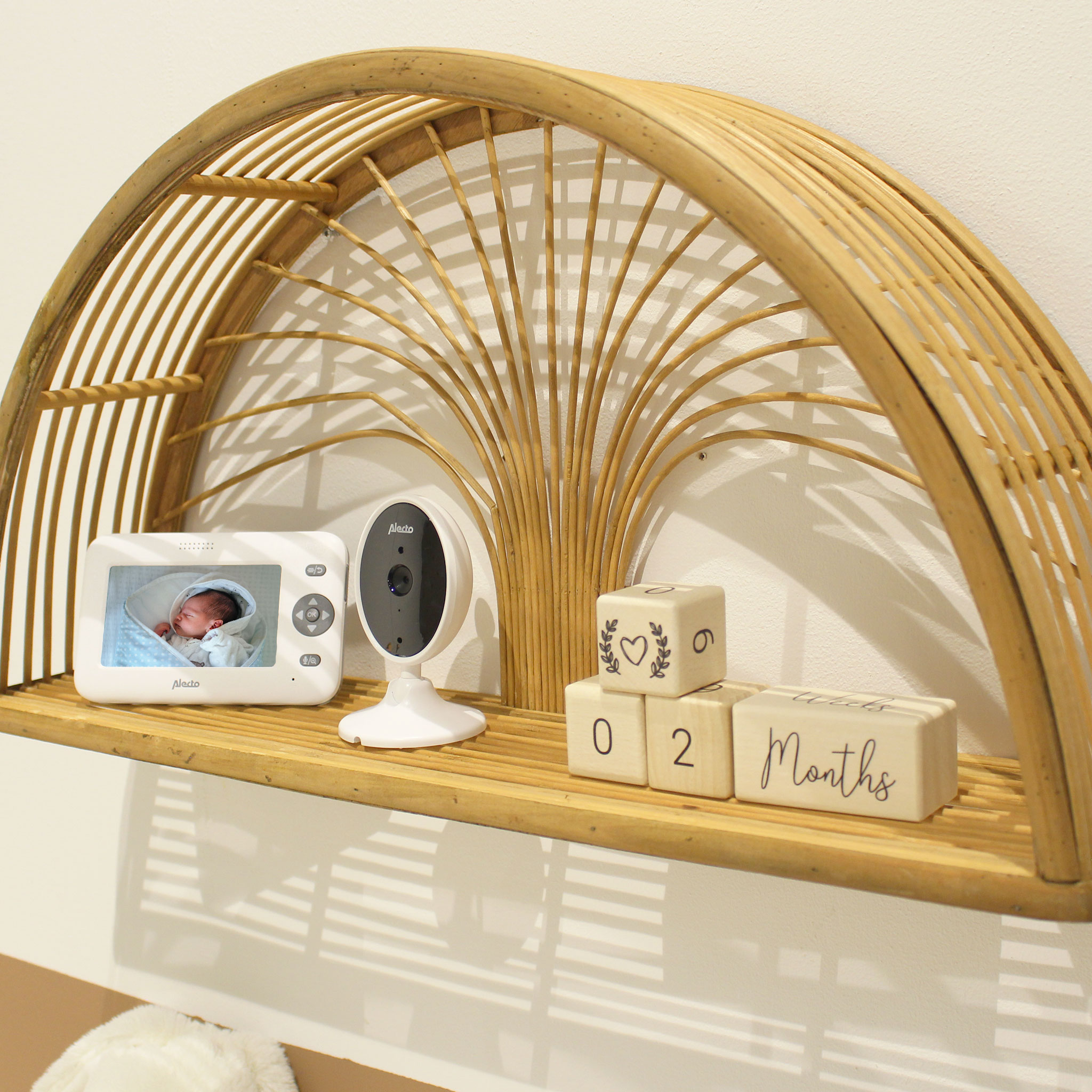 Shelf with a baby monitor, blocks showing months, and a decorative arched frame.