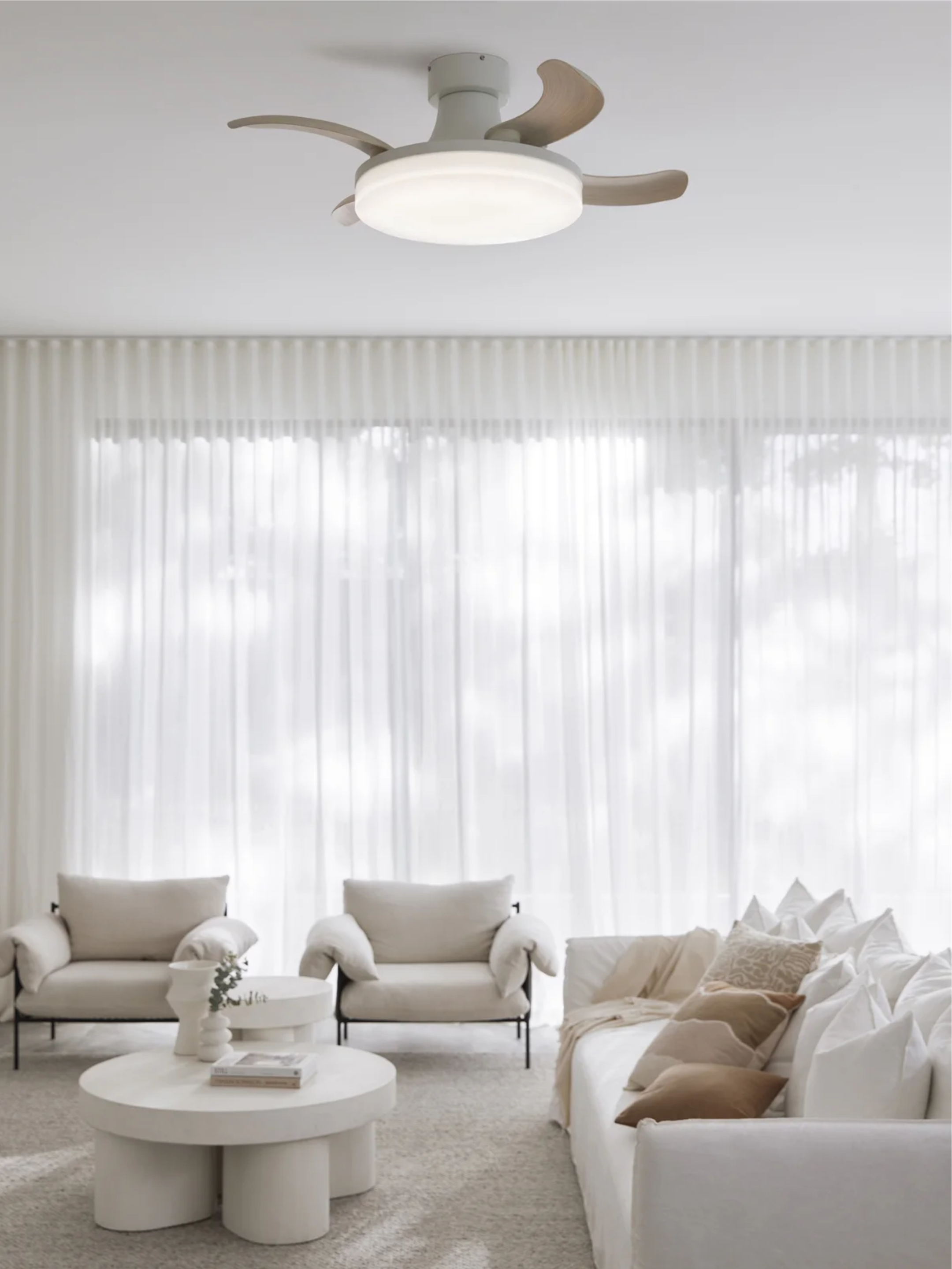 Wohnzimmer mit weißen Möbeln, rundem Couchtisch, zwei Sesseln und Deckenventilator. Vorhänge im Hintergrund.