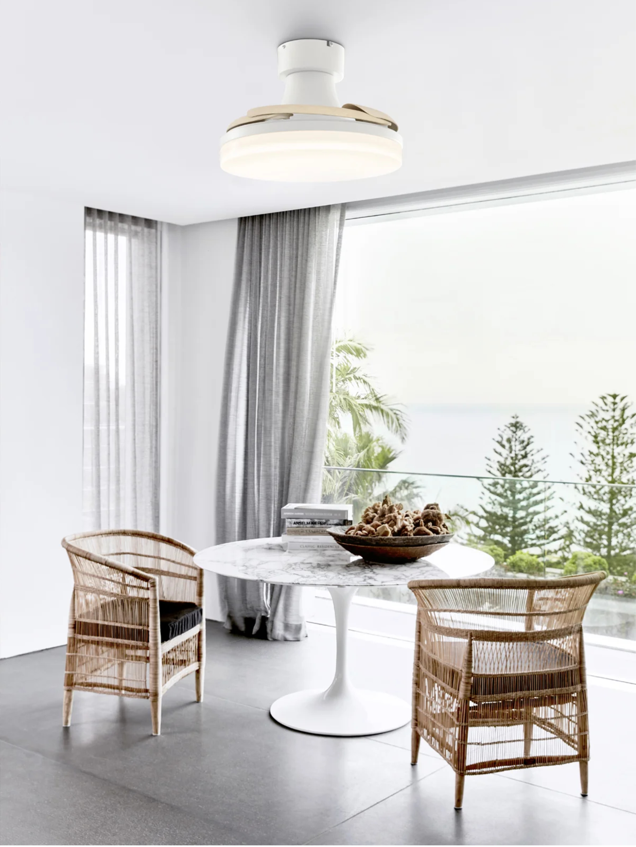 Ein moderner Essbereich mit Marmortisch, zwei Rattanstühlen und Deckenventilator. Fenster mit Meerblick.