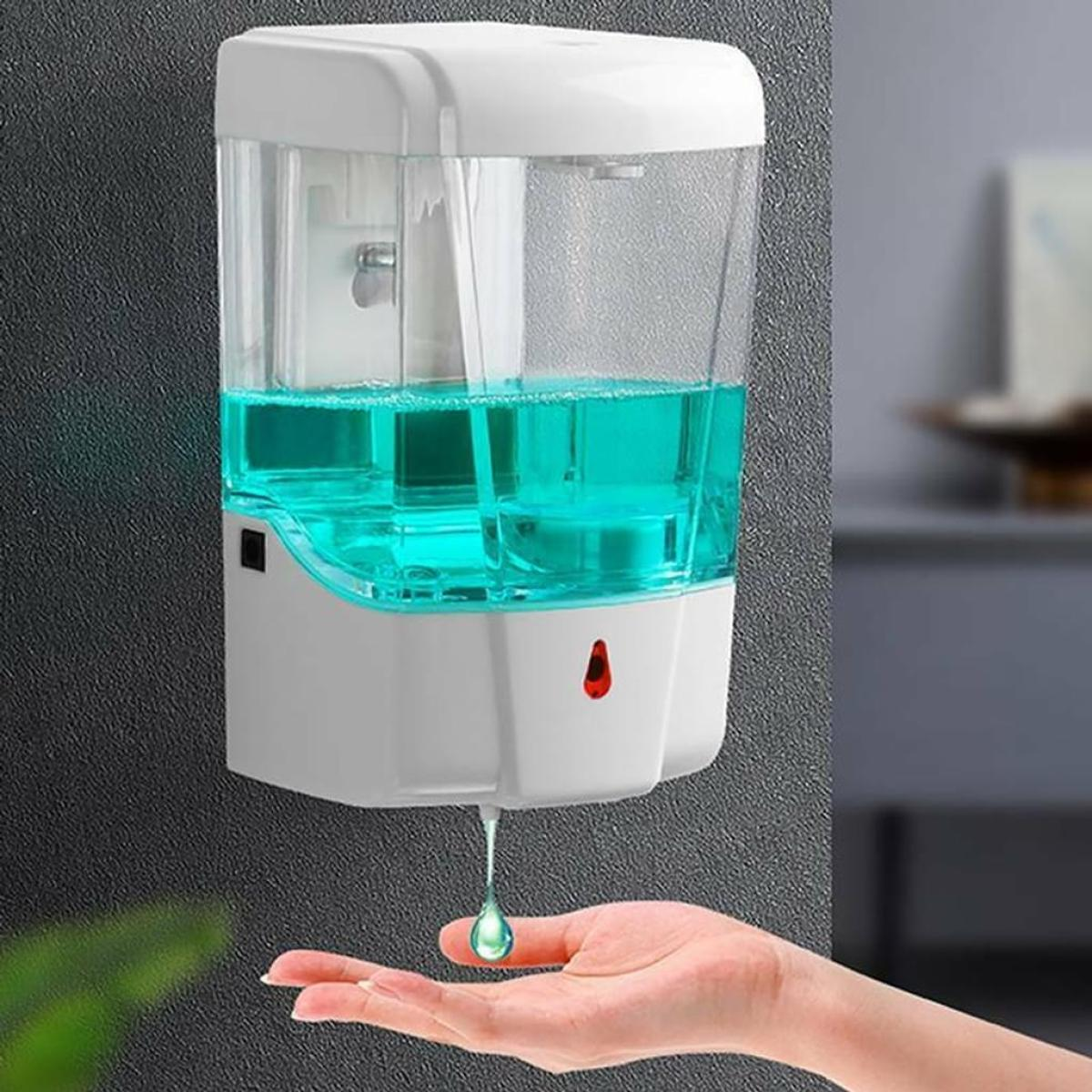 An der Wand befestigter weißer automatischer Seifenspender mit grüner Seife und Hand darunter. Grauer Hintergrund.