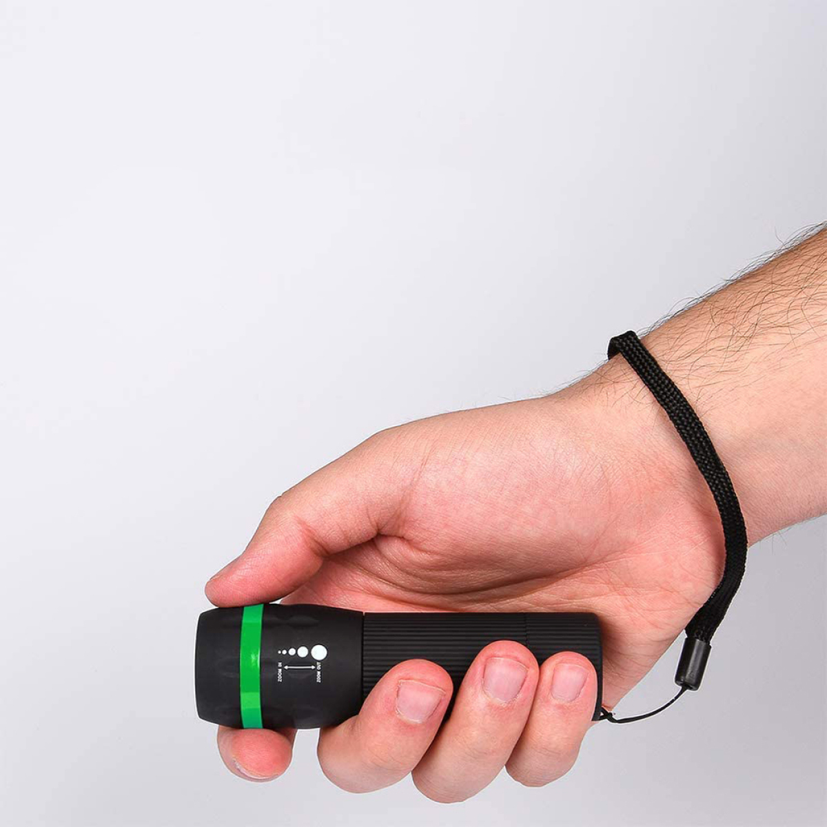 Hand hält eine schwarze Taschenlampe mit grünem Ring. Die Taschenlampe hat Zoom- und Lichtanzeige.