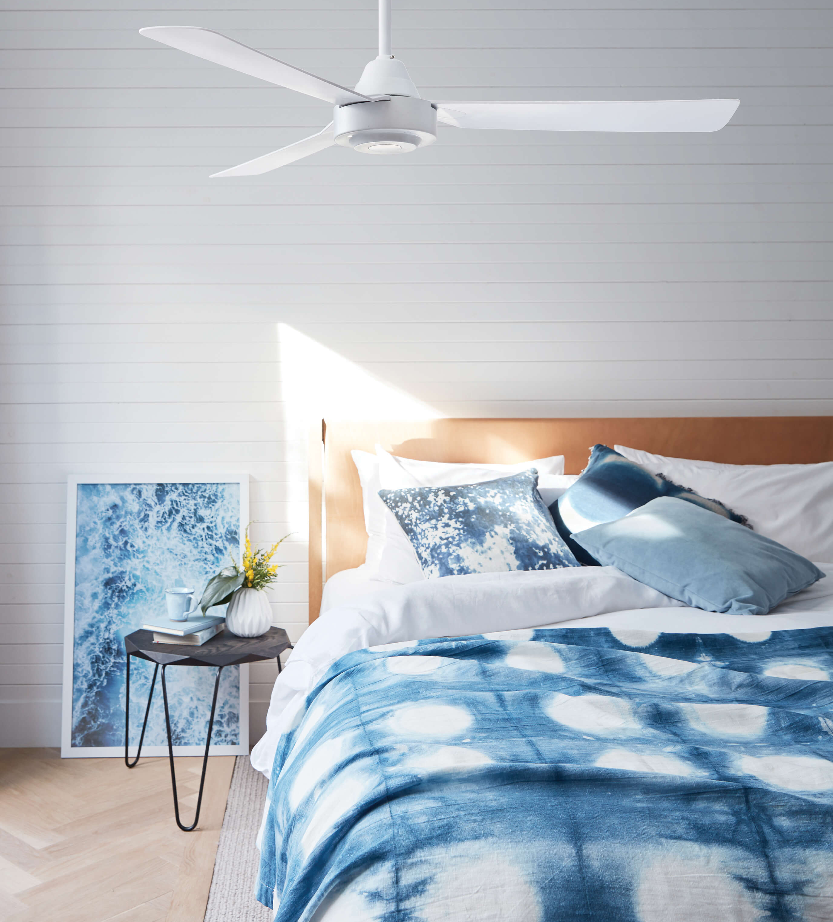 Camera da letto con ventilatore a soffitto, letto con coperta blu a fantasia, opere d'arte e comodino.