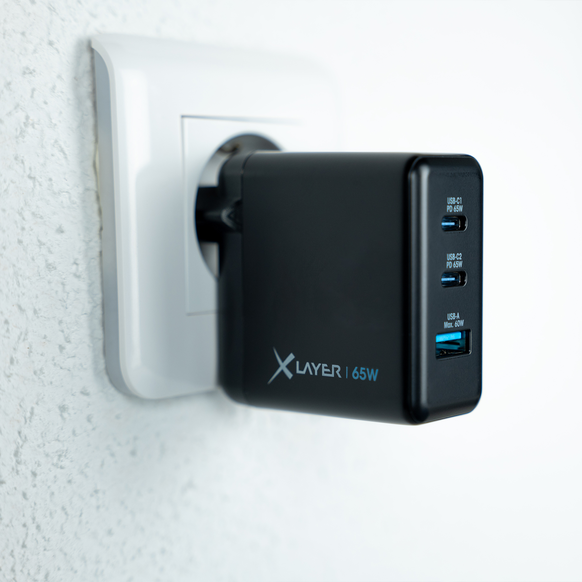Schwarzes USB-Wandladegerät, das in eine Steckdose gesteckt ist. Es hat drei USB-Anschlüsse und 65W.
