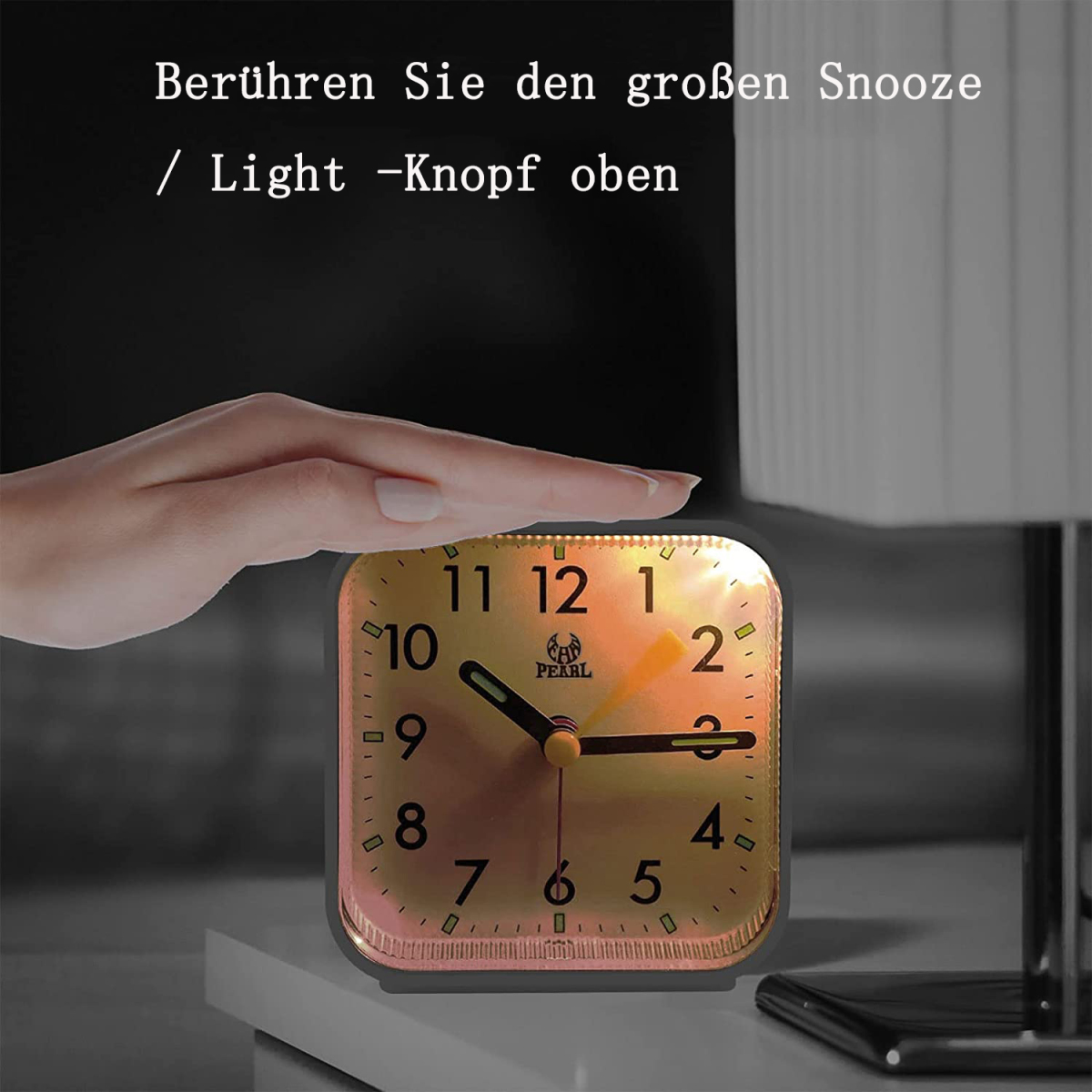 Ein goldener Wecker auf einer weißen Oberfläche. Eine Hand berührt ihn gleich.