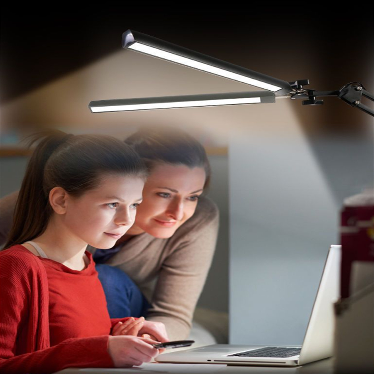 Ein Mädchen und eine Frau betrachten einen Laptop, mit einer Schreibtischlampe, die sie anstrahlt.