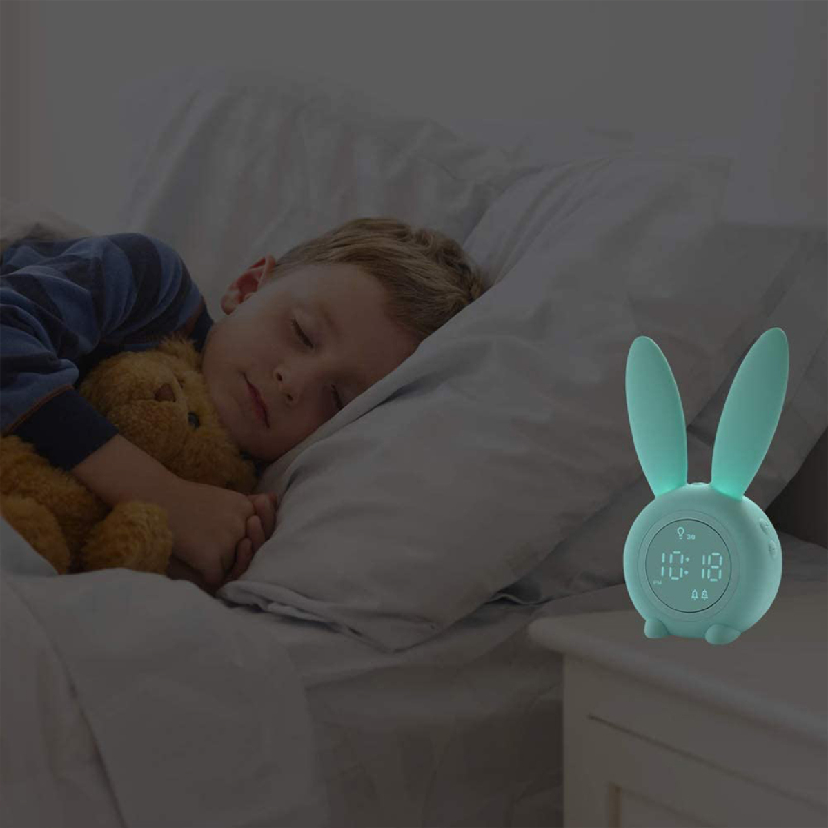 Schlafender Junge mit Teddybär neben einem hasenförmigen Wecker auf einem Nachttisch.