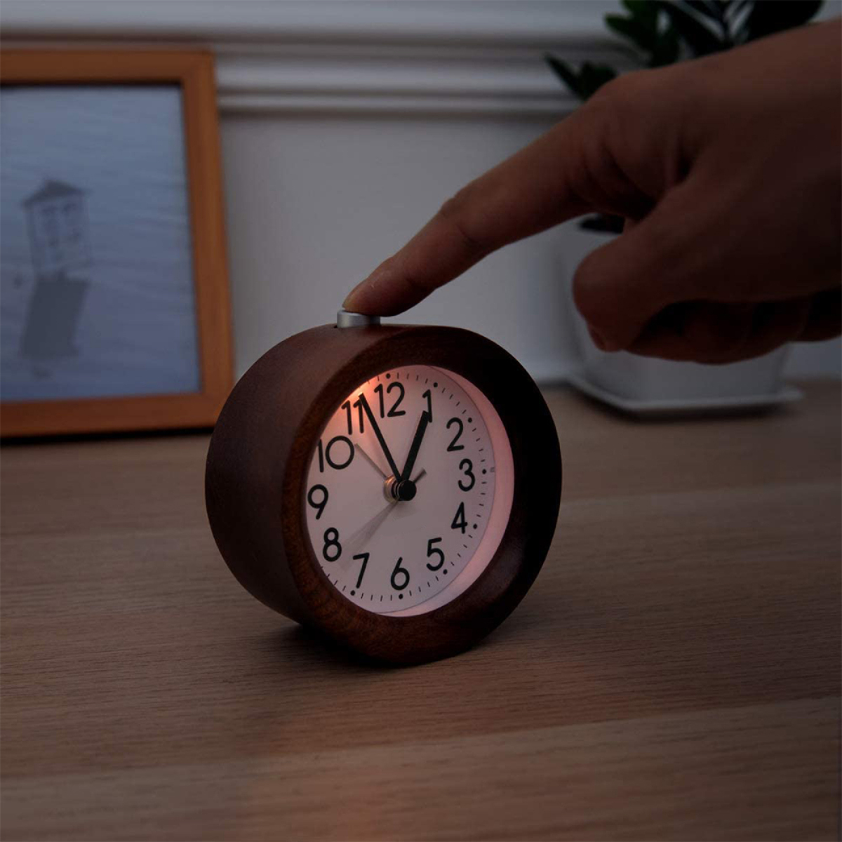Holzuhr mit beleuchtetem Zifferblatt. Ein Finger drückt einen Knopf an der Uhr.