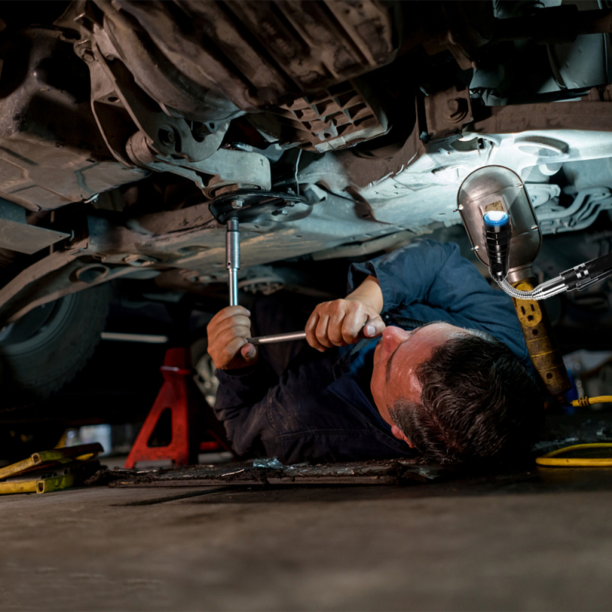Ein Mechaniker arbeitet unter einem Auto und verwendet einen Schraubenschlüssel und eine Lampe.