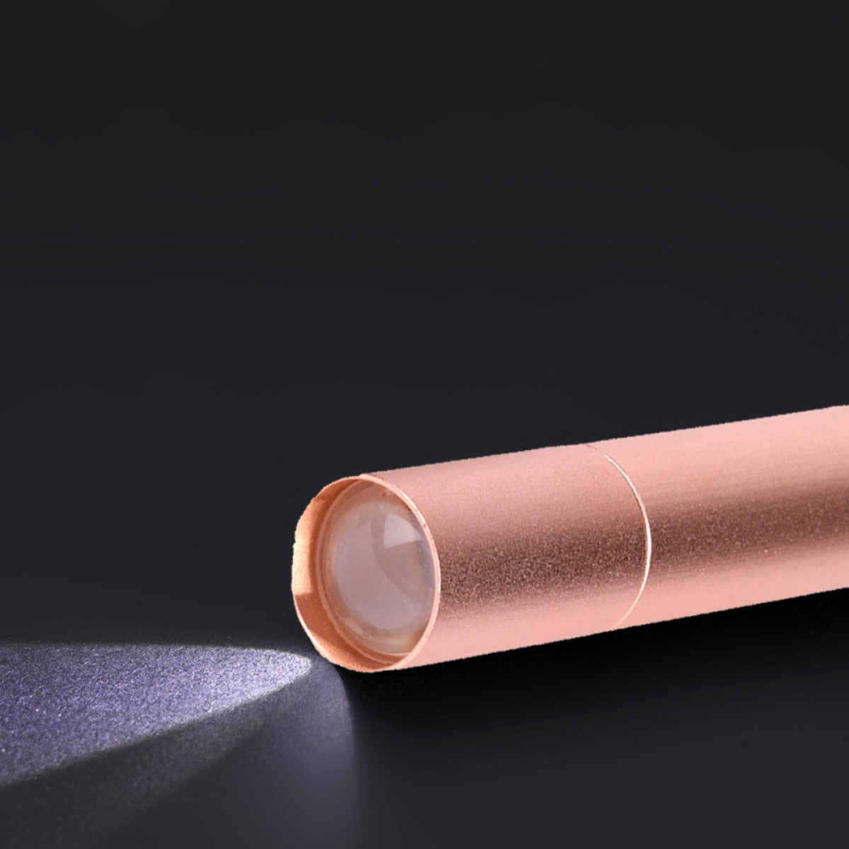 Roségoldene Taschenlampe, die Licht auf schwarzem Hintergrund abgibt.