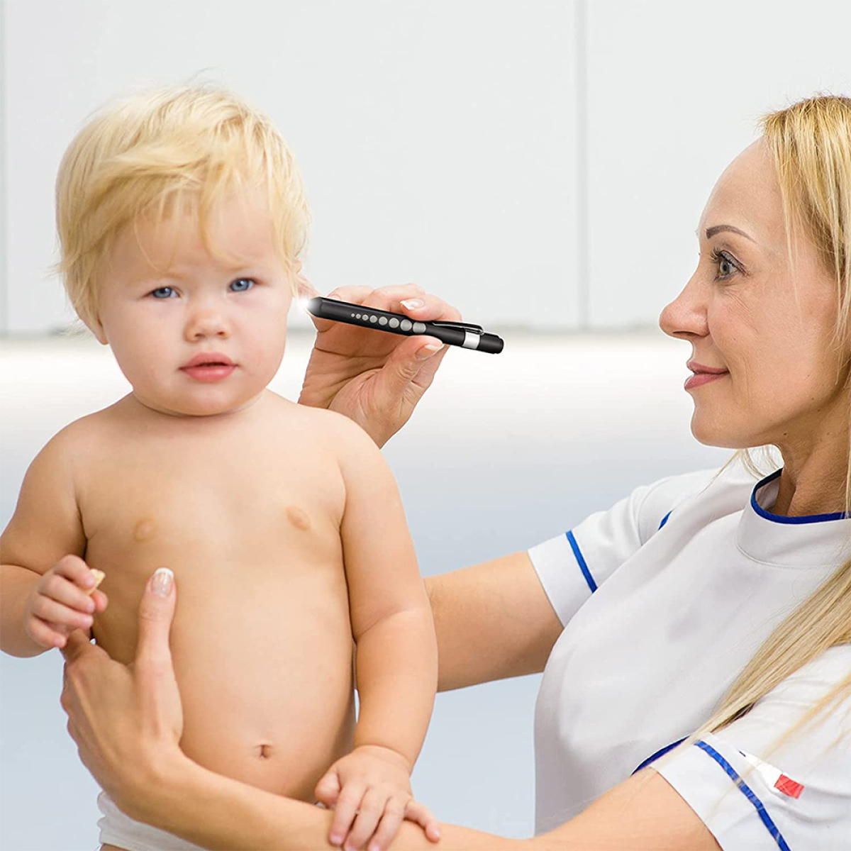 Ein Arzt untersucht das Ohr eines Babys mit einem Otoskop. Das Baby schaut in die Kamera. Weißer Hintergrund.