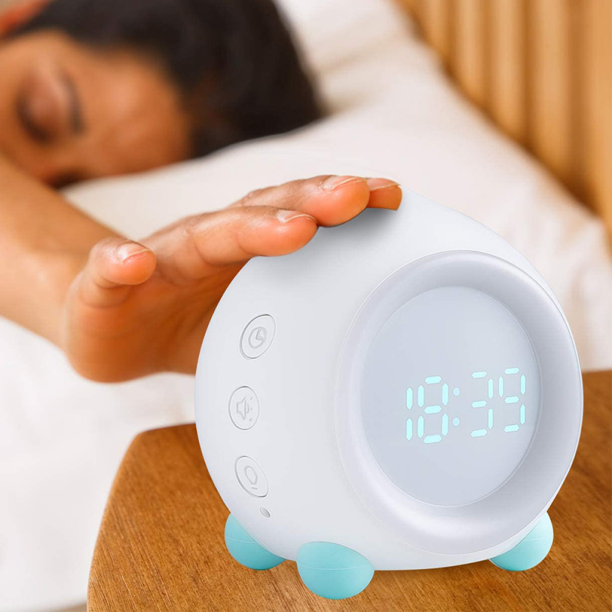 Weißer Wecker mit Digitalanzeige auf Holzoberfläche. Eine Hand greift danach.