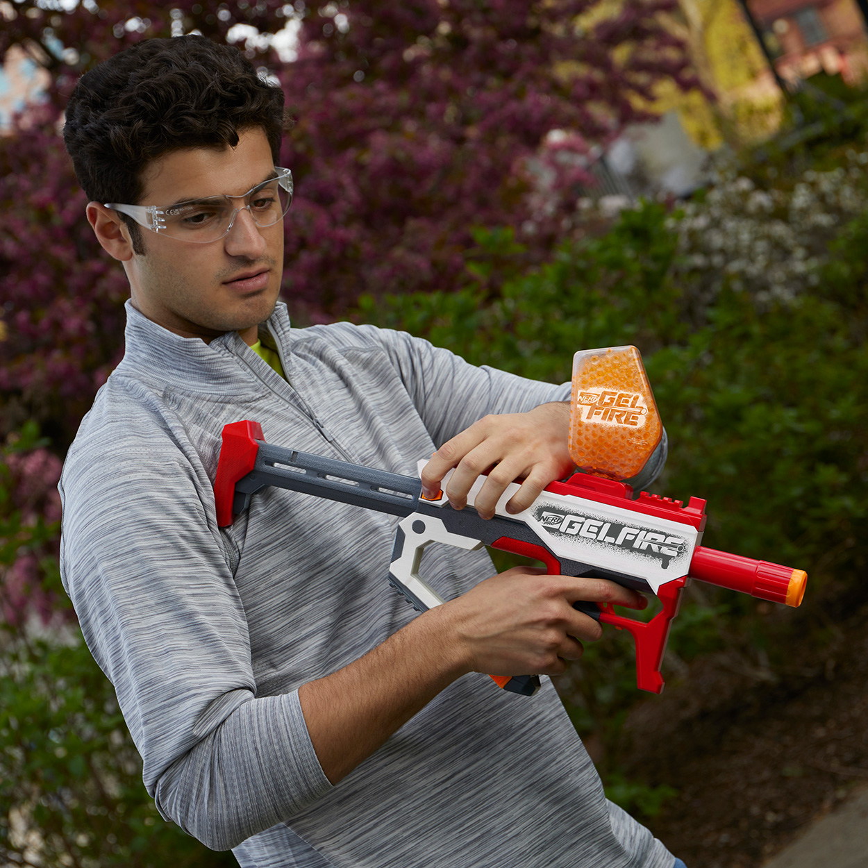 Mann hält eine Gel-Blaster-Pistole, trägt eine Schutzbrille, im Freien.