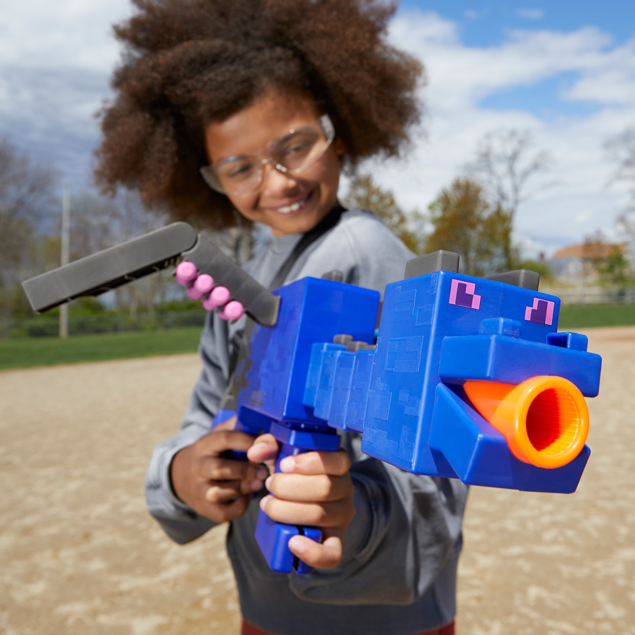 Un bambino che tiene in mano una pistola giocattolo, blu con canna arancione. Il bambino sorride e indossa occhiali di sicurezza.