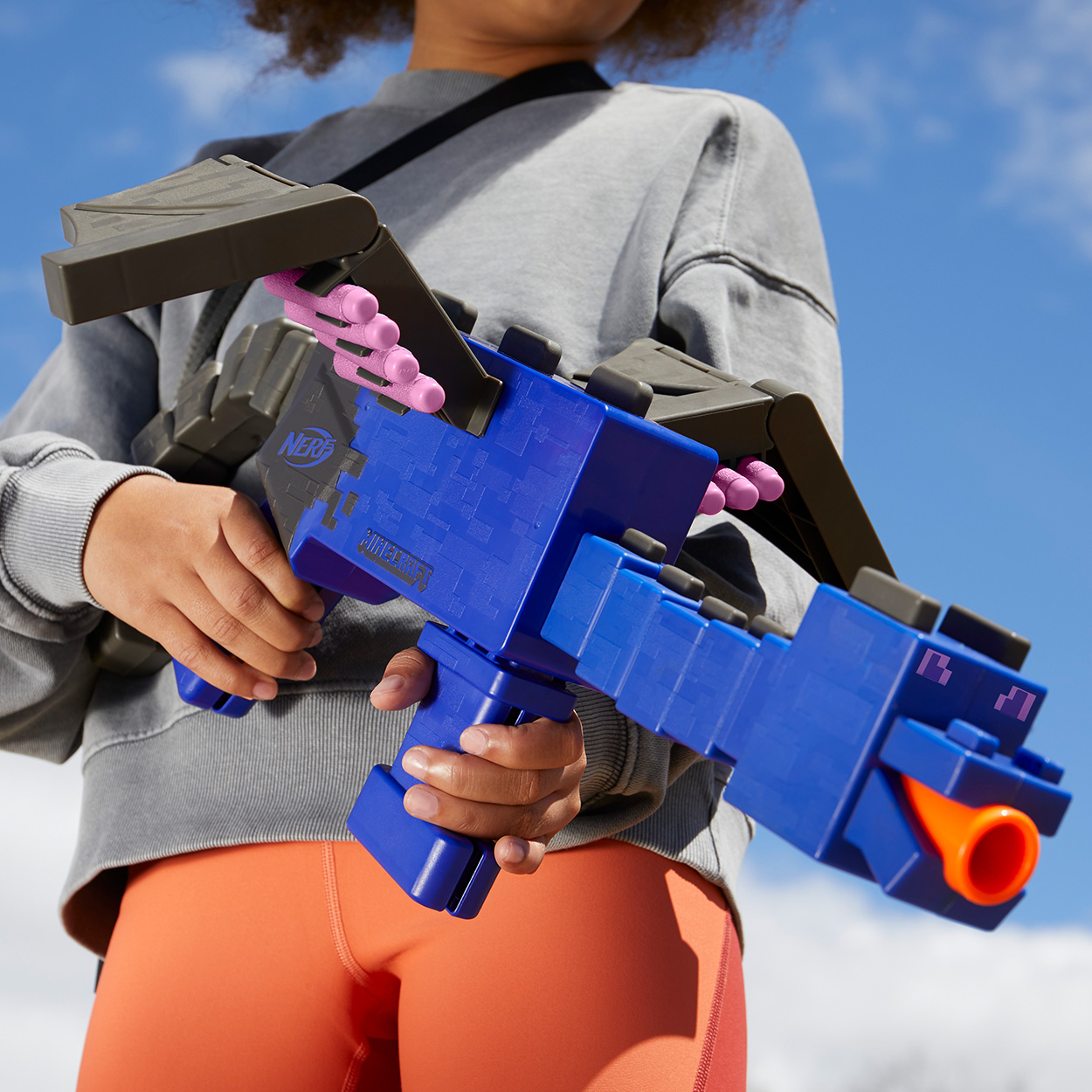 Bambino che tiene una pistola giocattolo blu. La pistola è blu e ha dettagli arancioni. Contro cielo blu.