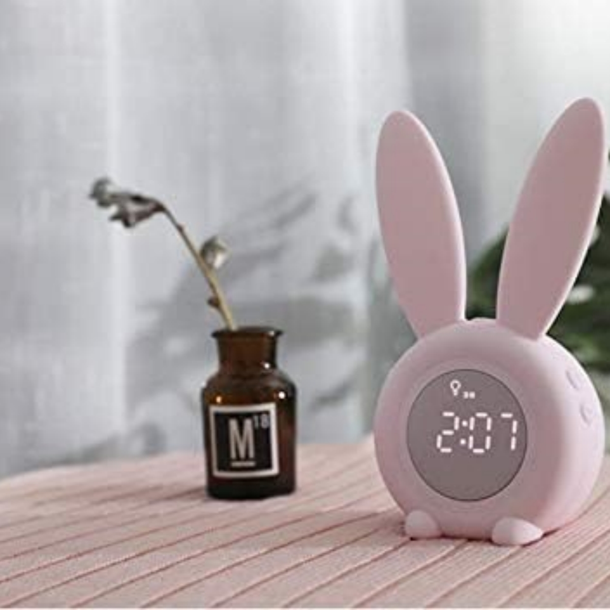 Ein rosa hasenförmiger Wecker, der 2:07 anzeigt, mit einer Vase im Hintergrund.