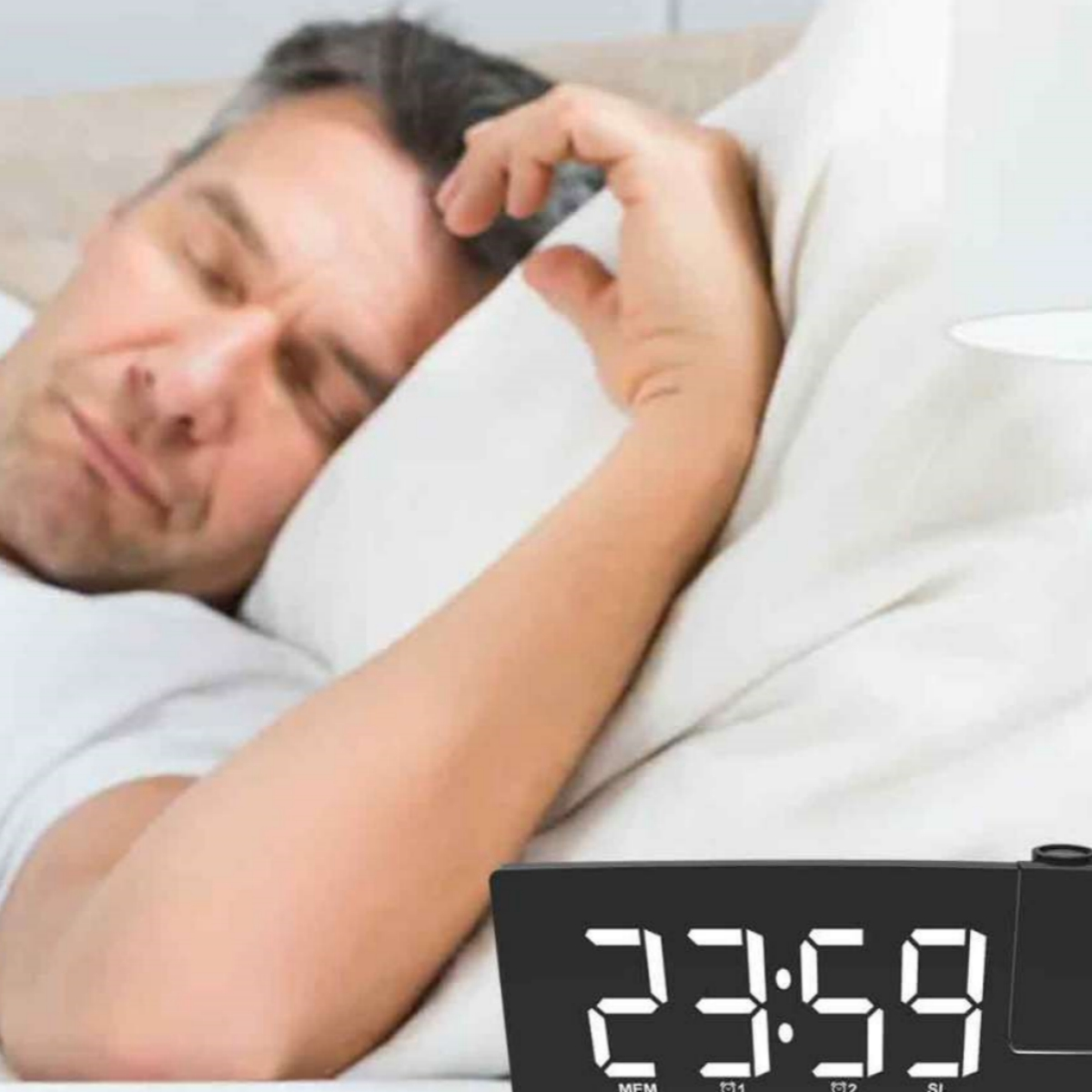 Mann schläft im Bett mit einer Digitaluhr in der unteren Ecke. Die Uhr zeigt 23:59.