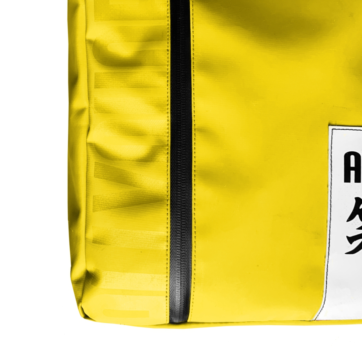 Primer plano de una bolsa amarilla con cremallera negra y etiqueta blanca con caracteres japoneses.