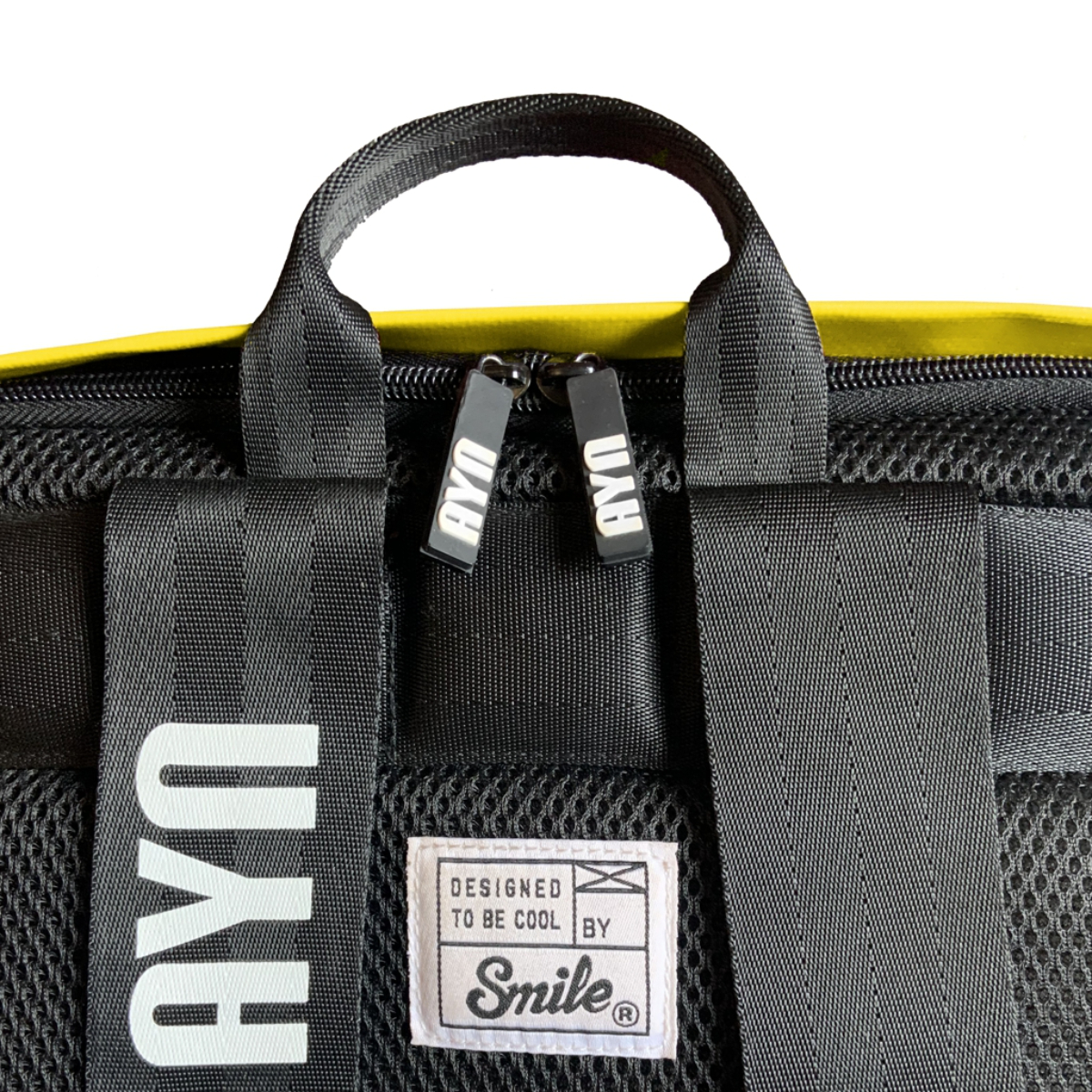 Mochila negra con detalles amarillos. Las correas tienen el logo AYU. La etiqueta dice 'Designed to be cool'.