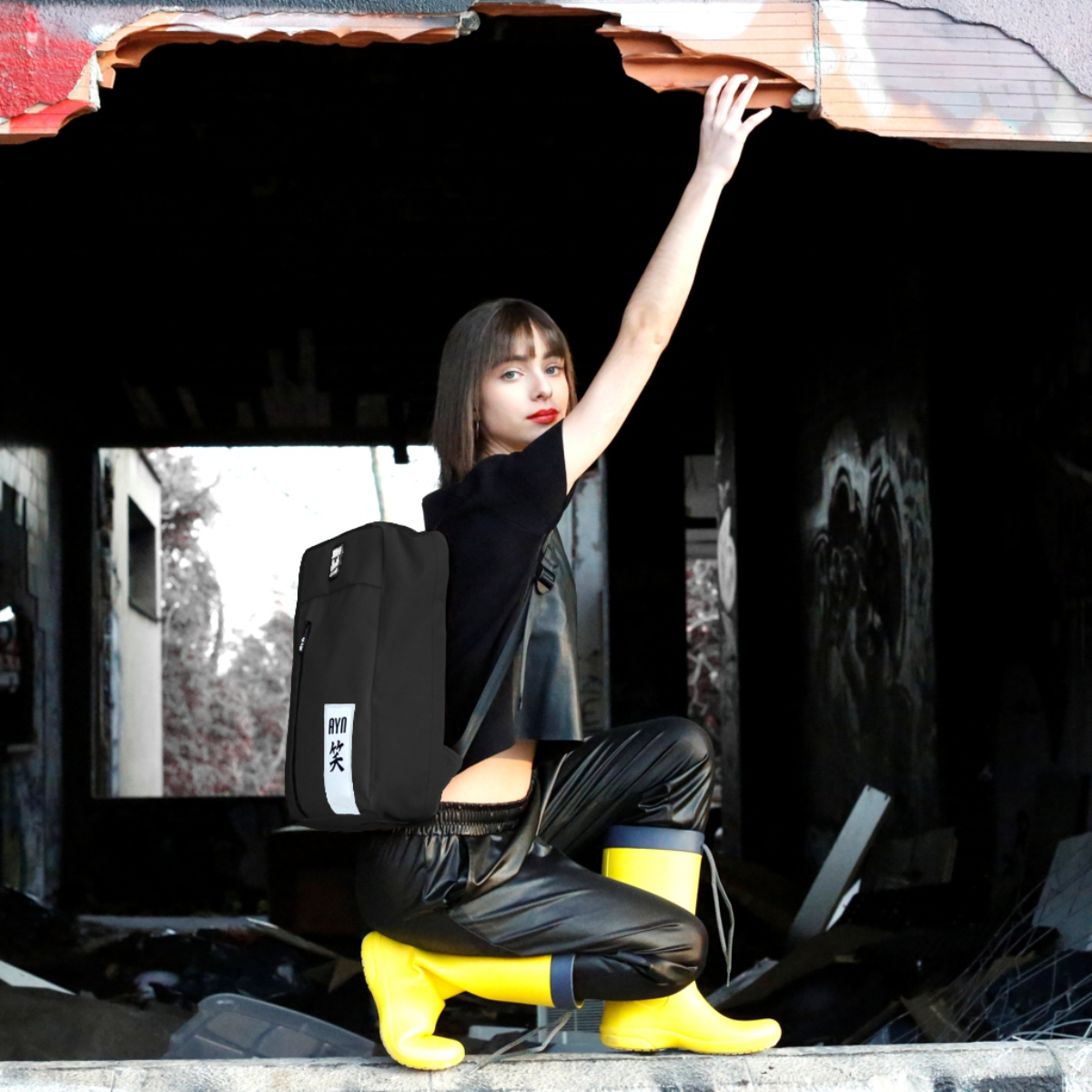 Una mujer vestida de negro con mochila negra y botas amarillas.