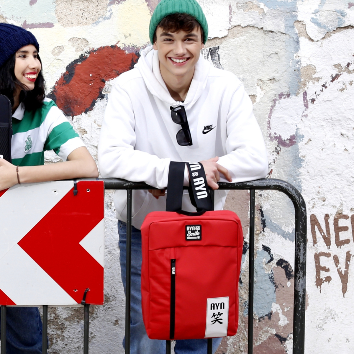 Dos personas con una bolsa roja, apoyadas en una valla. La bolsa tiene un logo.