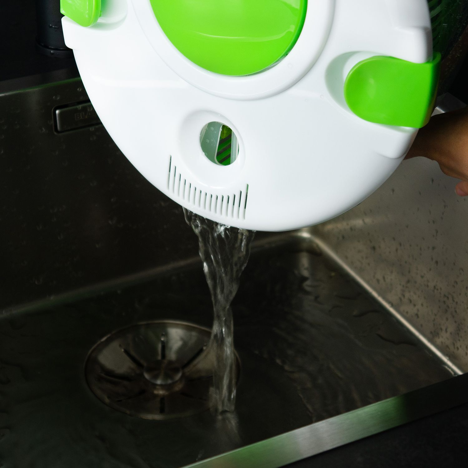 Wasser fließt aus einem weiß-grünen Objekt in ein Edelstahlbecken.
