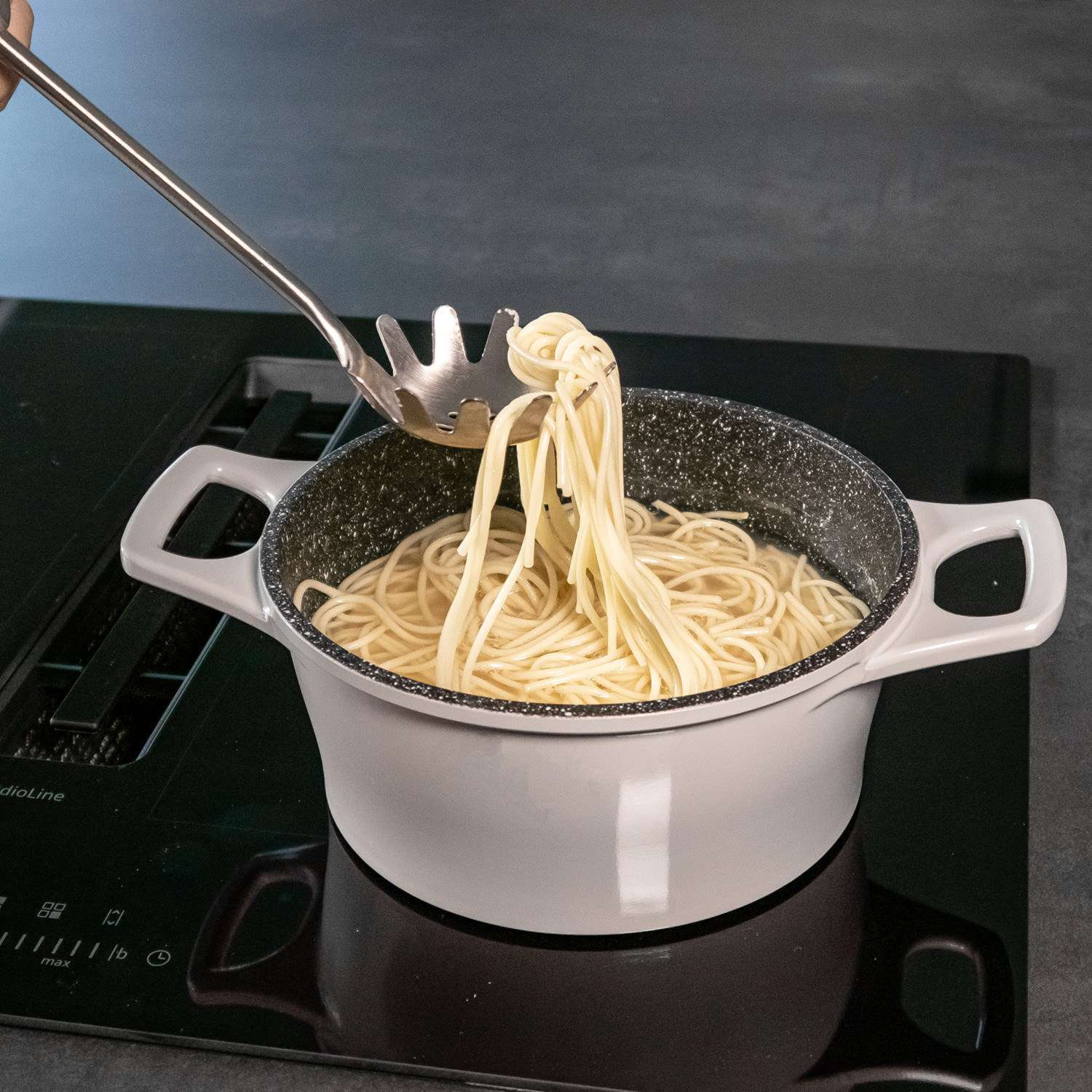 Spaghetti werden mit einem Schaumlöffel aus einem Topf mit kochendem Wasser auf einem Herd gehoben.