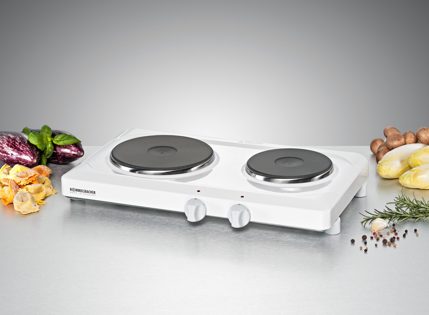 Biała podwójna płyta grzejna i warzywa na metalowej powierzchni. Dwie strefy gotowania.