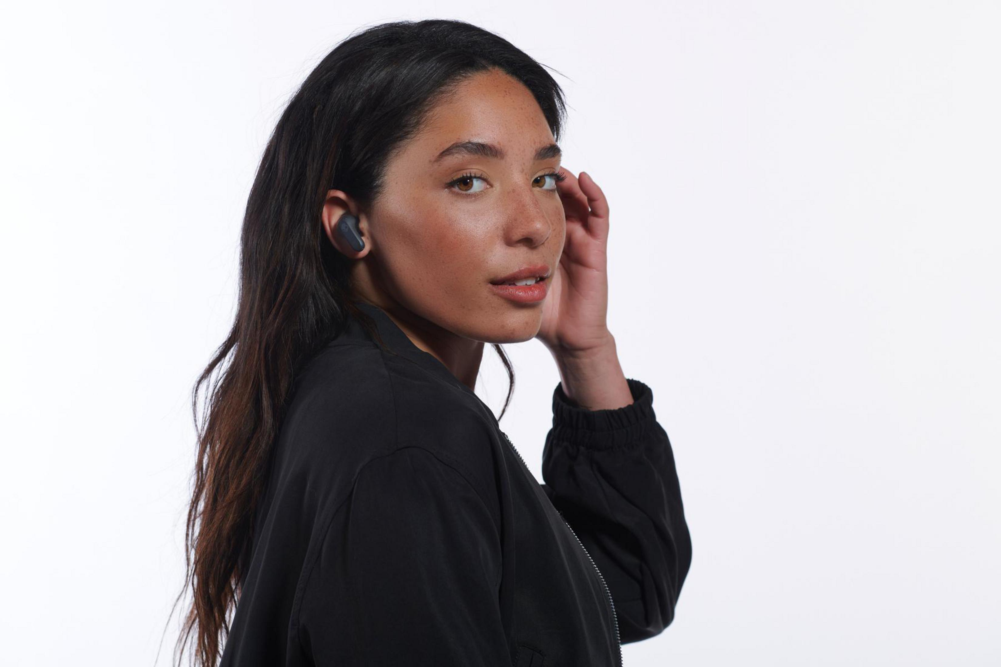 Kobieta z ciemnymi włosami w czarnej kurtce i słuchawkach.